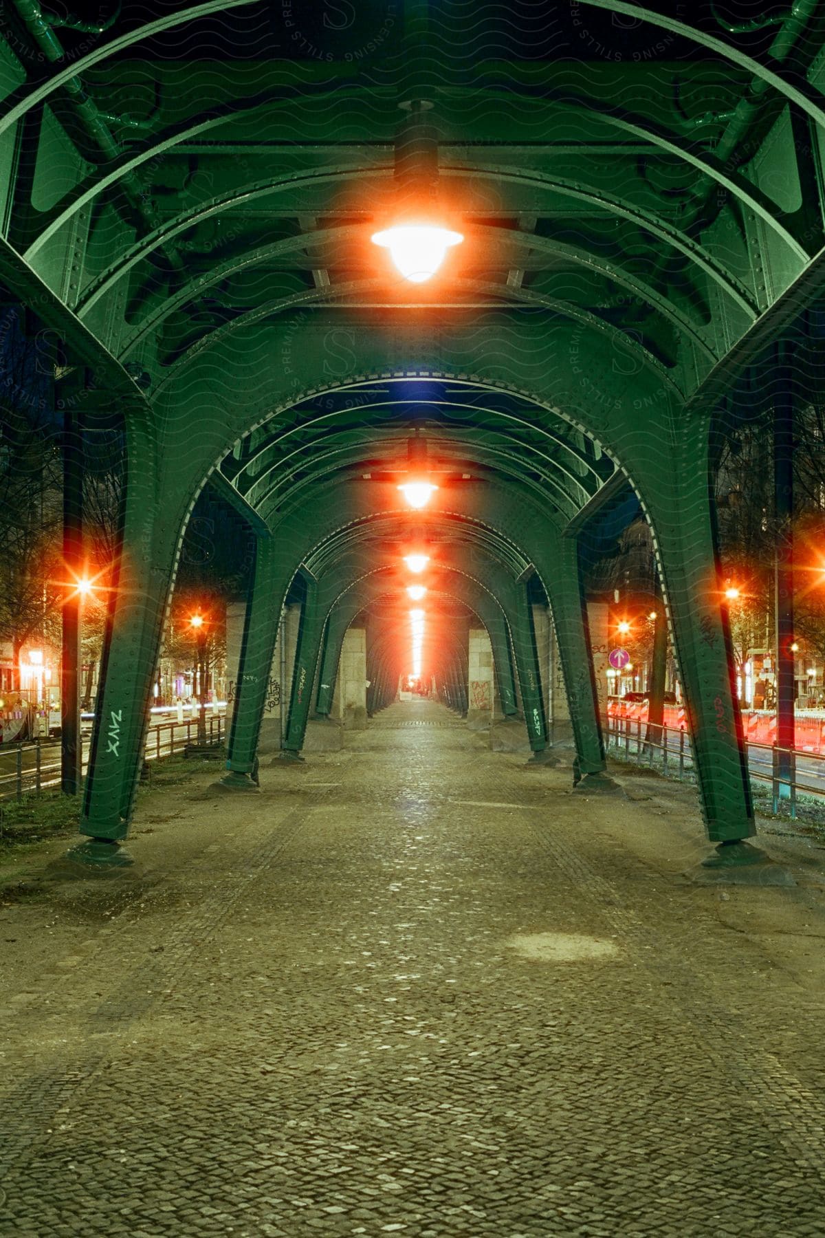 Green metallic arch with lights suspended on a concrete street with cobblestones in the city at night.