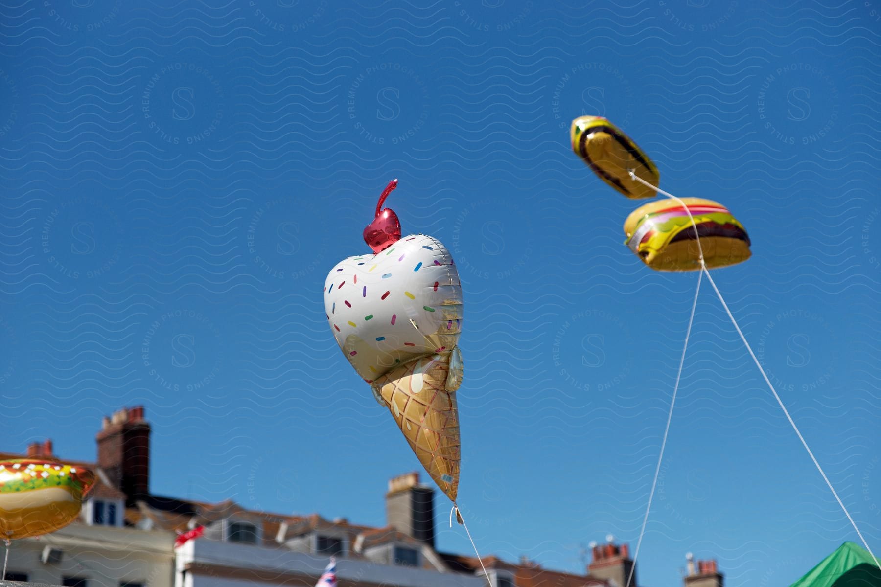 A bunch of festive balloons shaped like a hot dog, a hamburger, and an ice cream cone float together in the air.