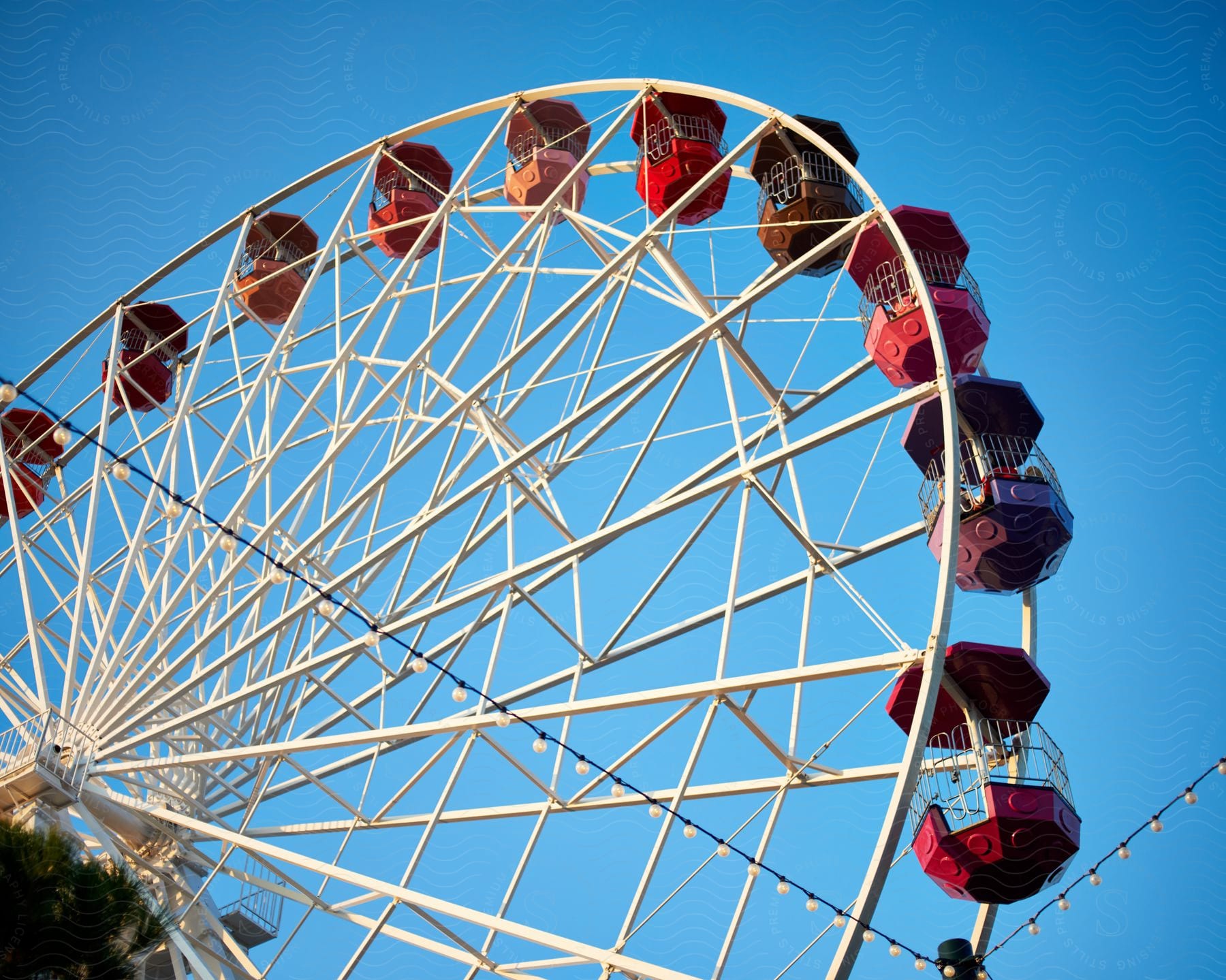 Colorful Ferris wheel cars contrast with the blue sky.