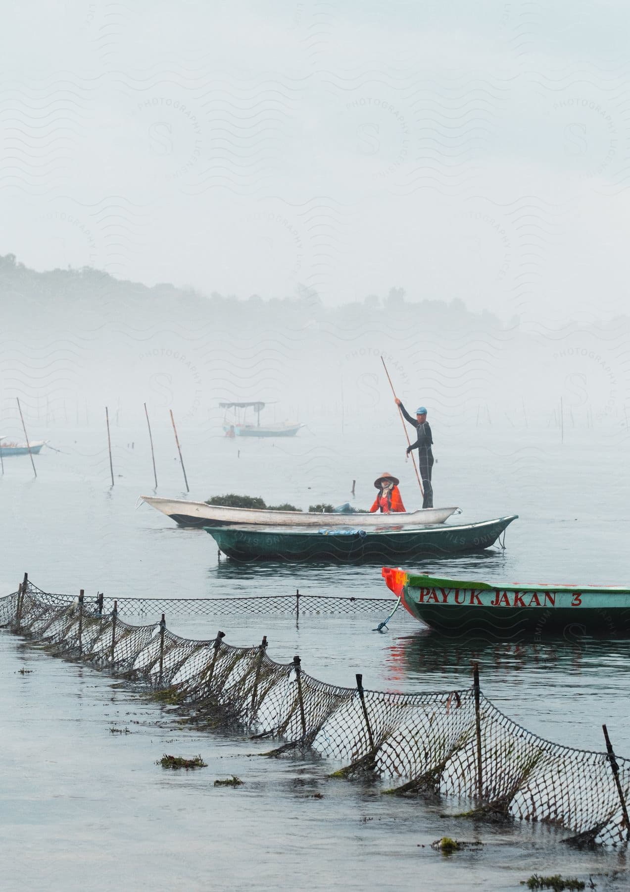 Two fishermen in a boat sailing through calm waters with submerged fishing nets alongside.