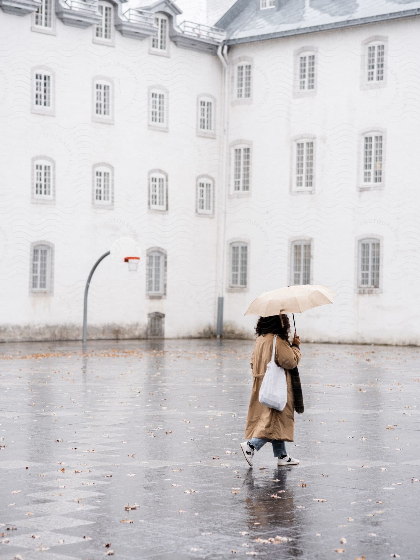 A woman walking on a wet street infront of a white building