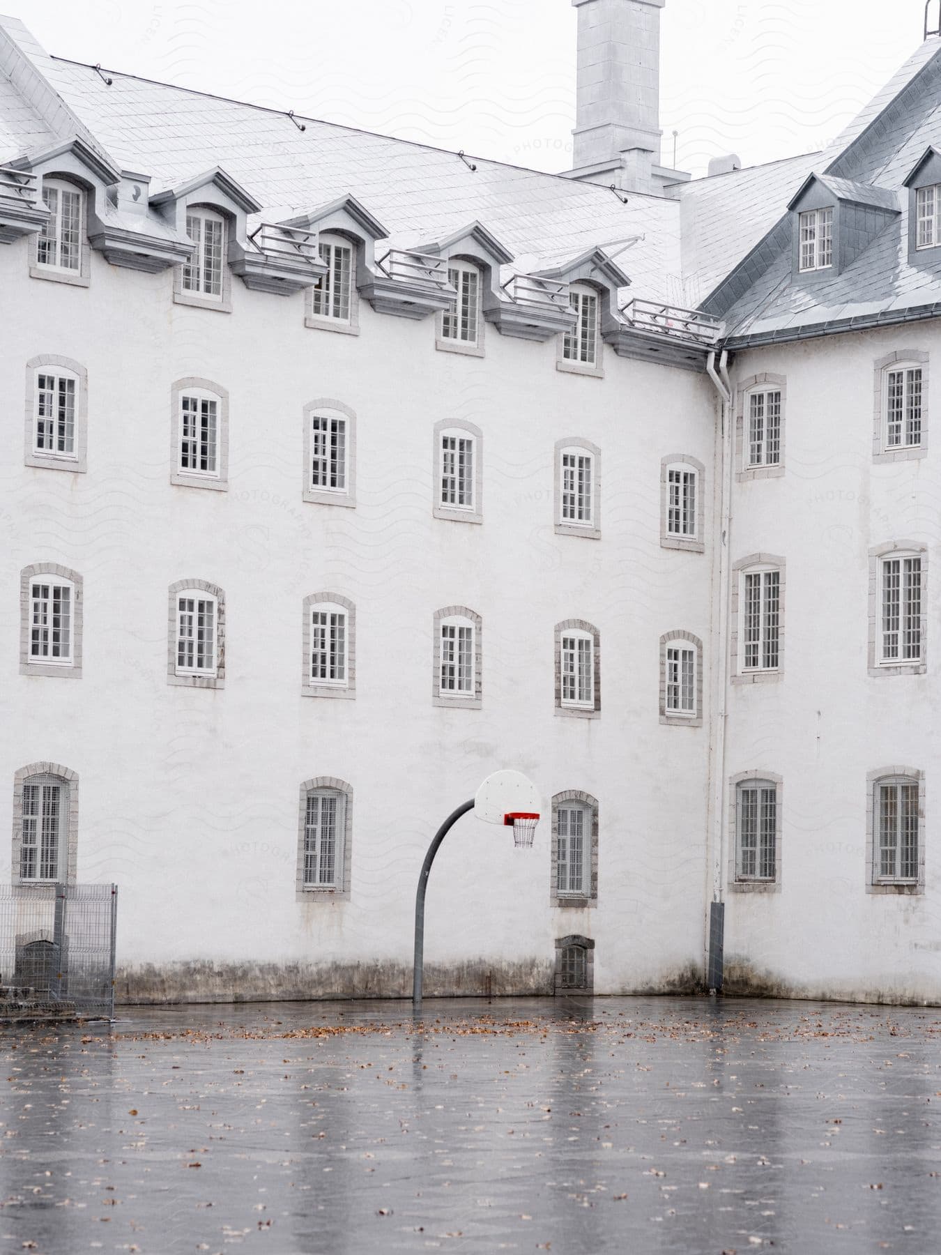 A white building with many windows and outside there is a basketball court with a wet floor