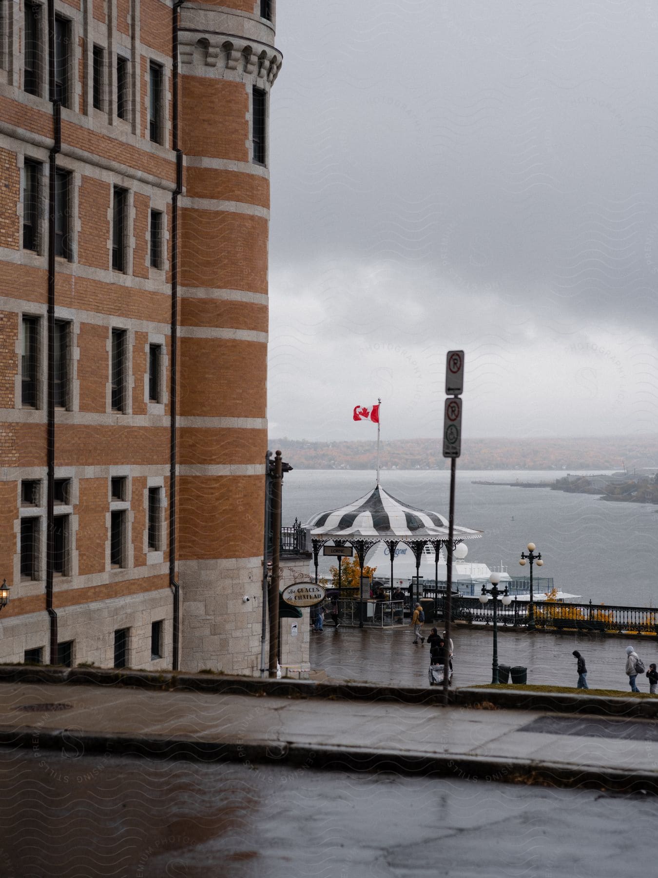 A cloudy day in a coastal town, a Canadian flag waving and a gazebo next to a body of water.