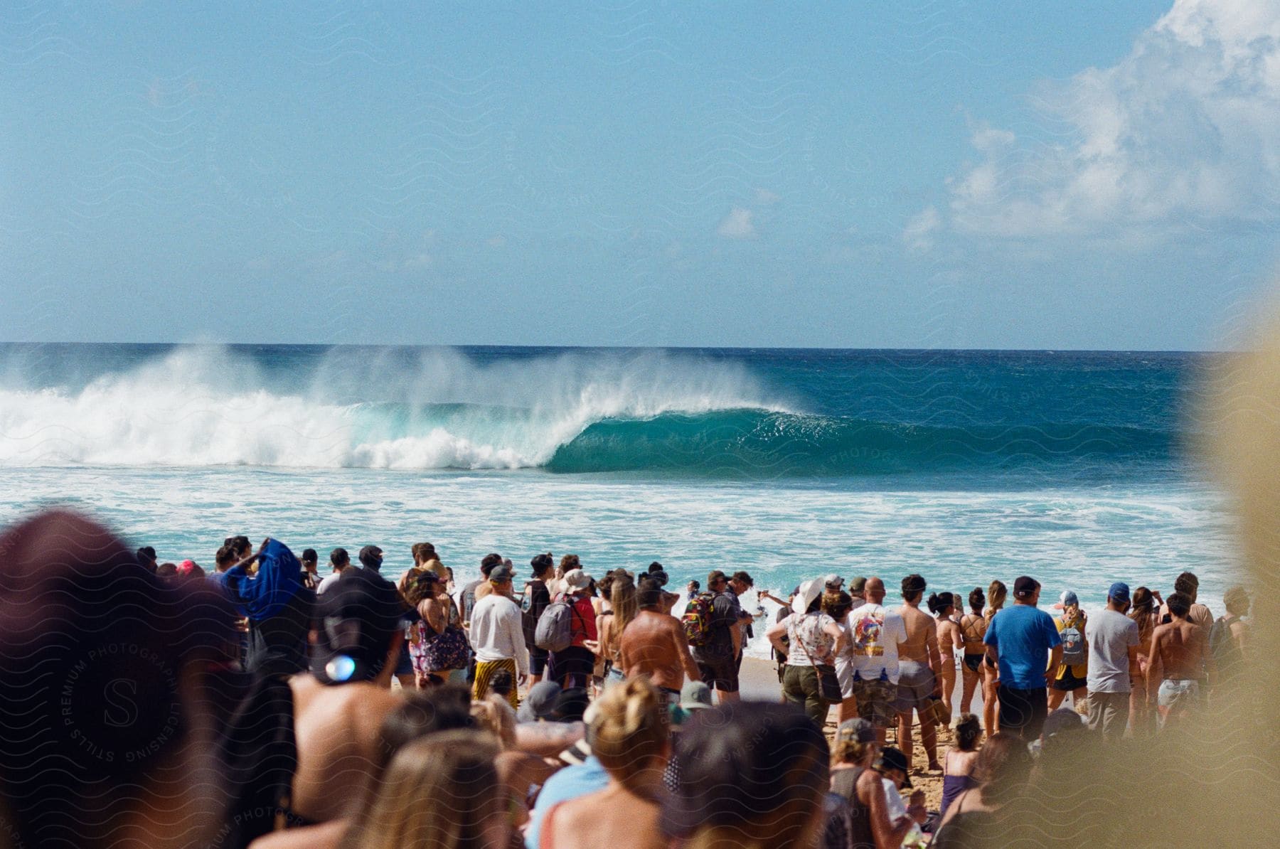 A large crowd on the beach looking at large waves in the water.