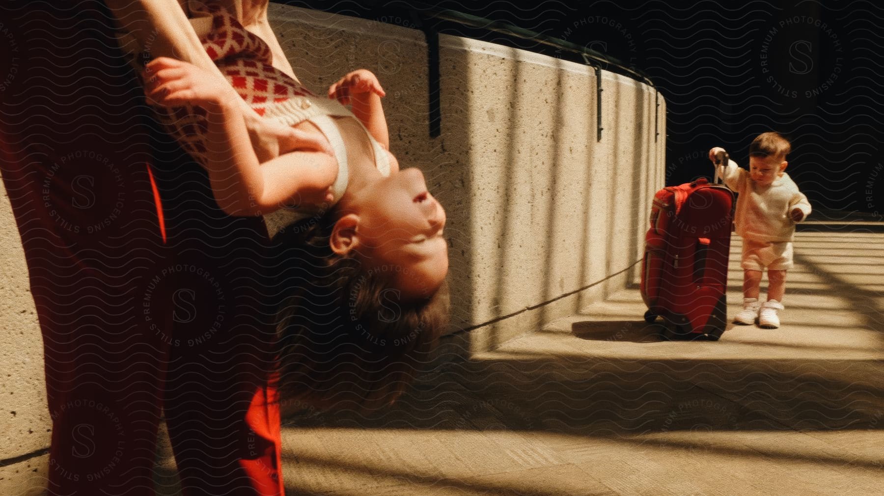 Boy holds luggage handle while his parent plays with his sister.