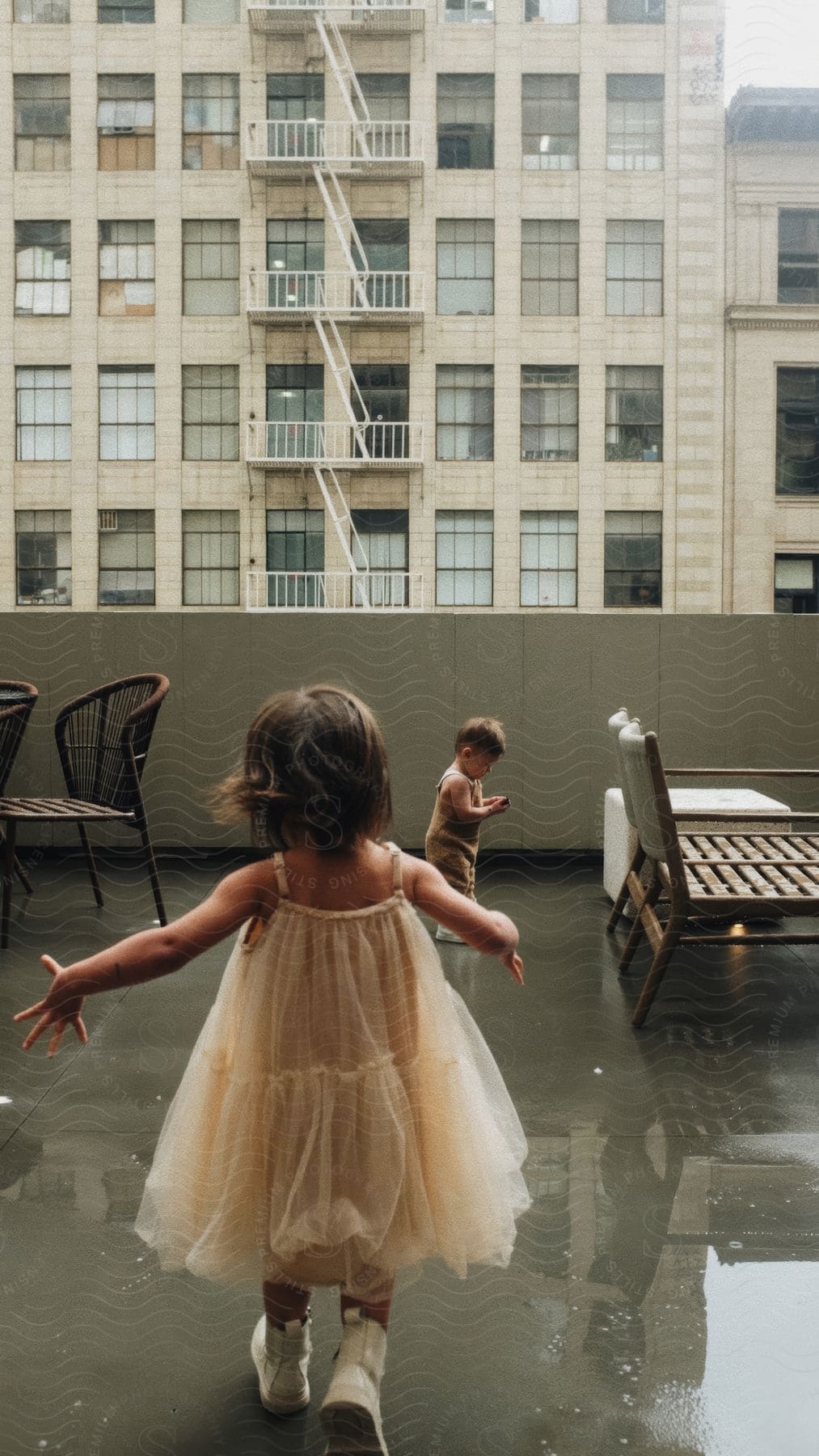 Two children play on a wet roof with a tall building in the background.