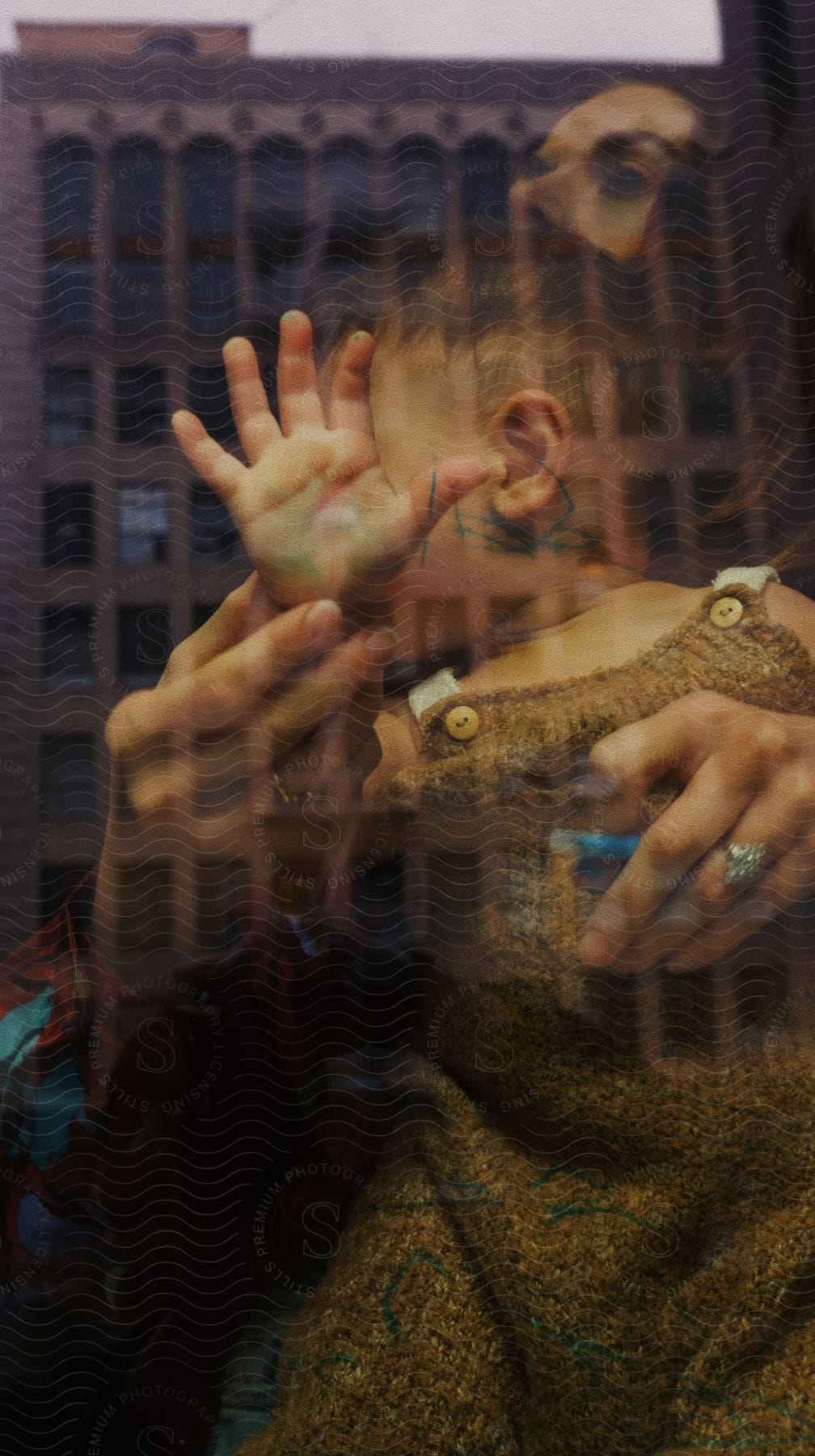 Mother holds daughter near glass reflecting nearby building.