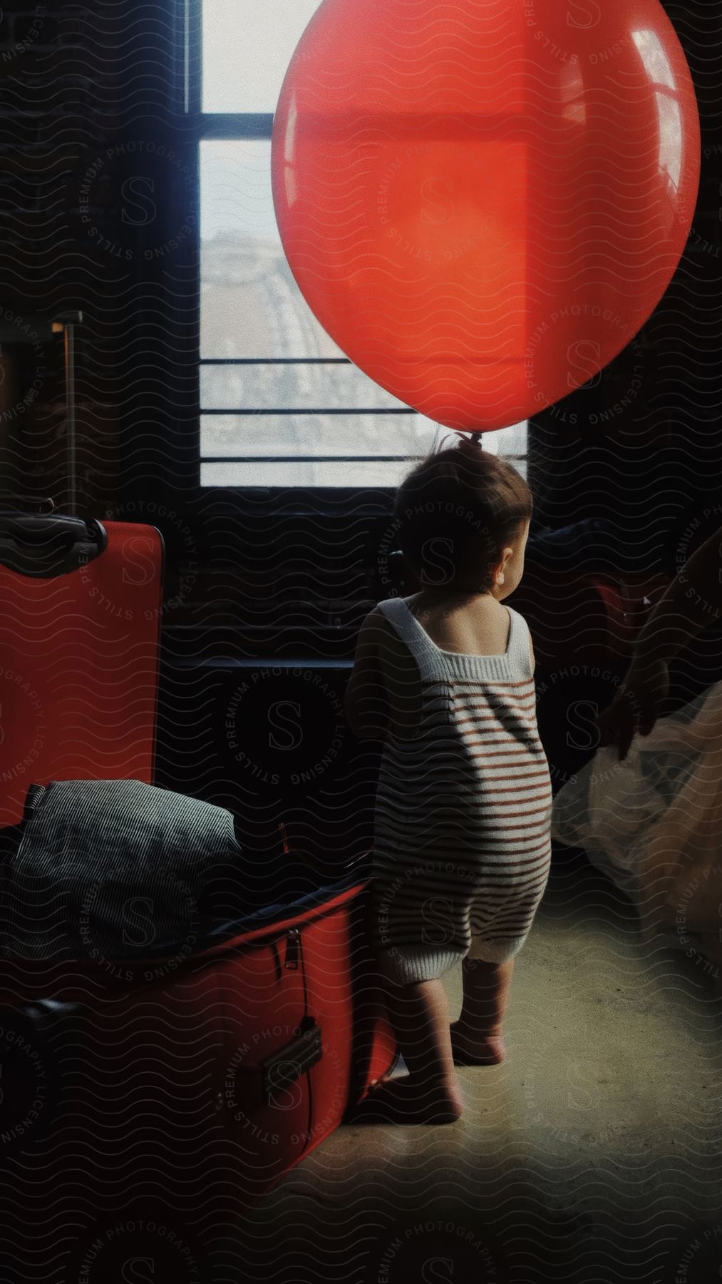 A child holds a large red balloon near a window.