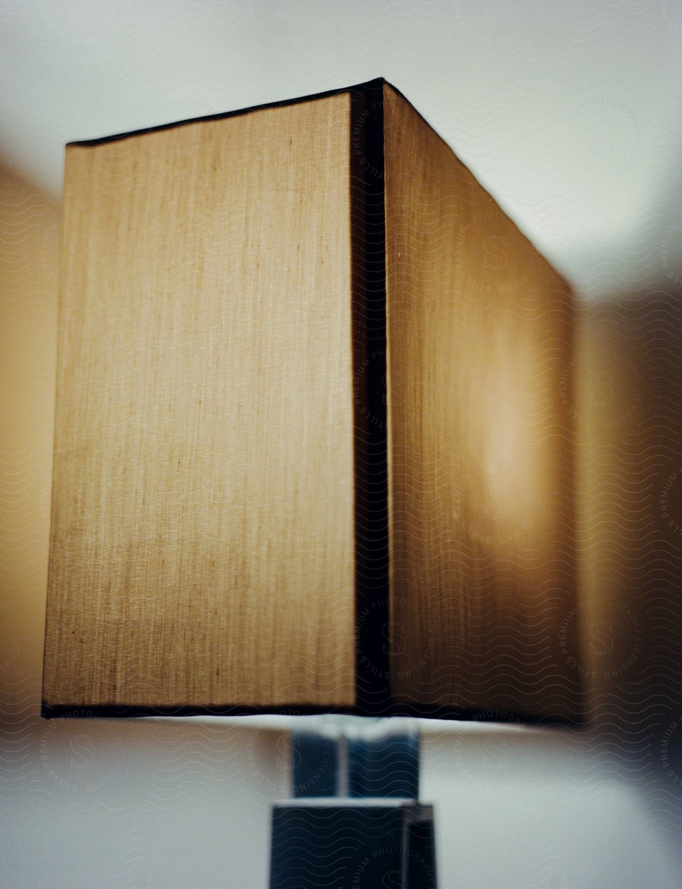 A lampshade with a square, textured dome in shades of beige. The dome appears to be made of fabric and rests on a gray, metallic base.