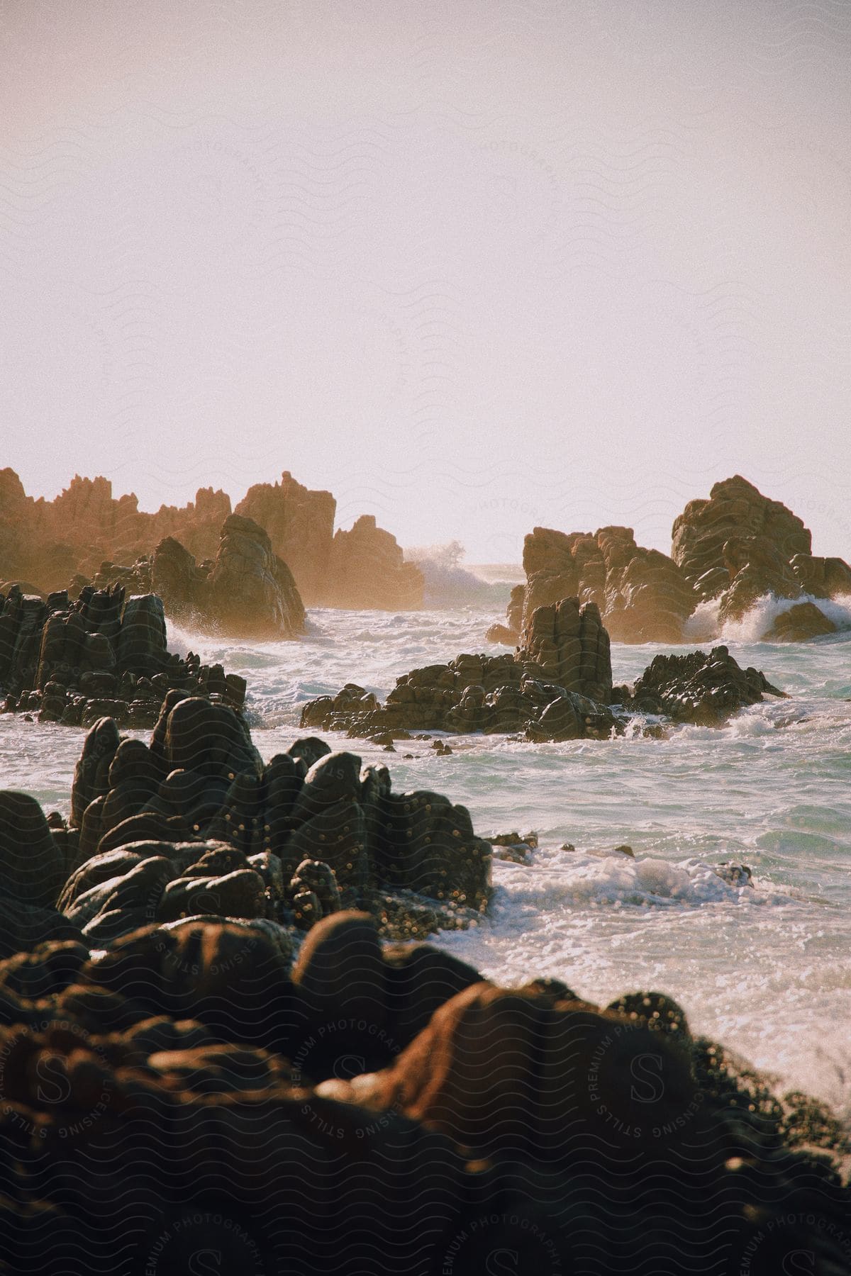 A rocky terrain in the ocean is battered by waves during the day.