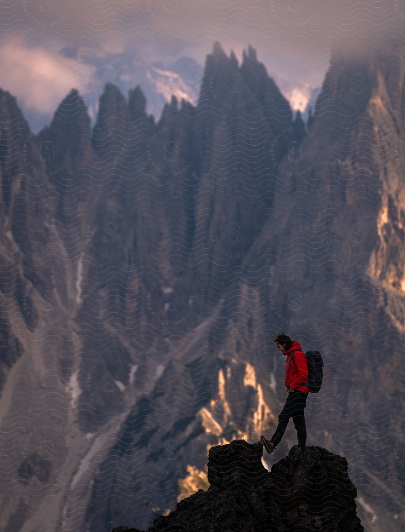 Hiker wearing a backpack standing on the peak of a mountain with snow covered mountains in the distance