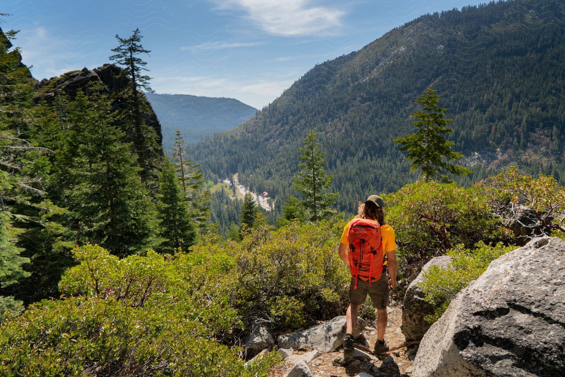 A hiker stands on a mountain trail that overlooks a road below it.