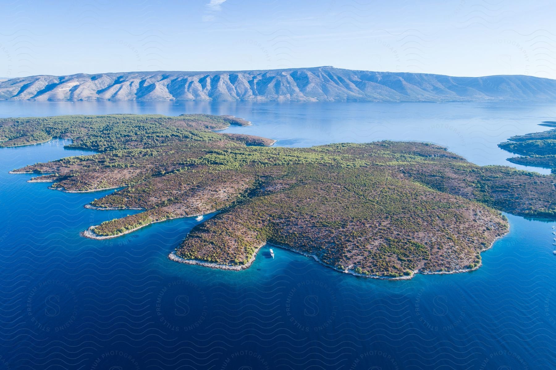 A breathtaking aerial of a green peninsula surrounded by the serene blue waters of a lake, with mountains in the background.