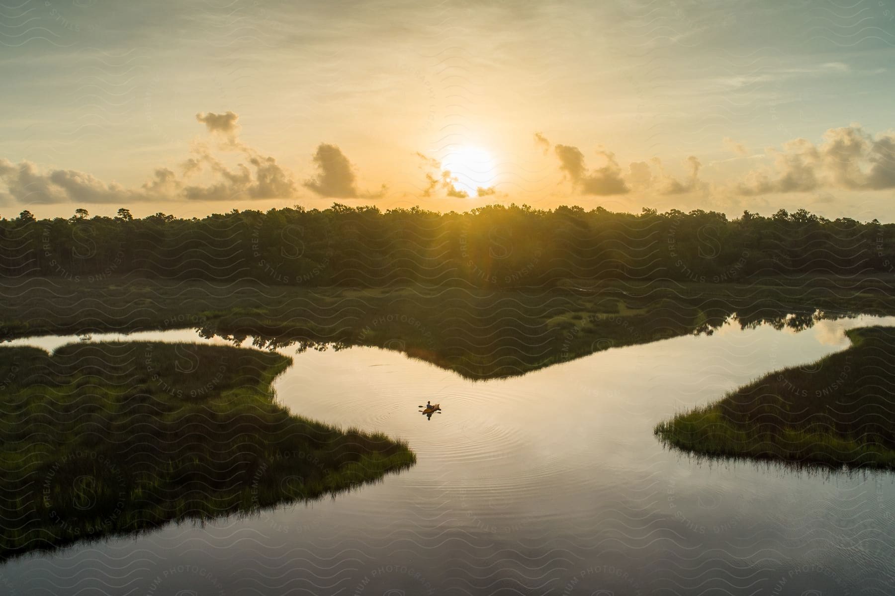 A person is kayaking in the river while the sun is setting.