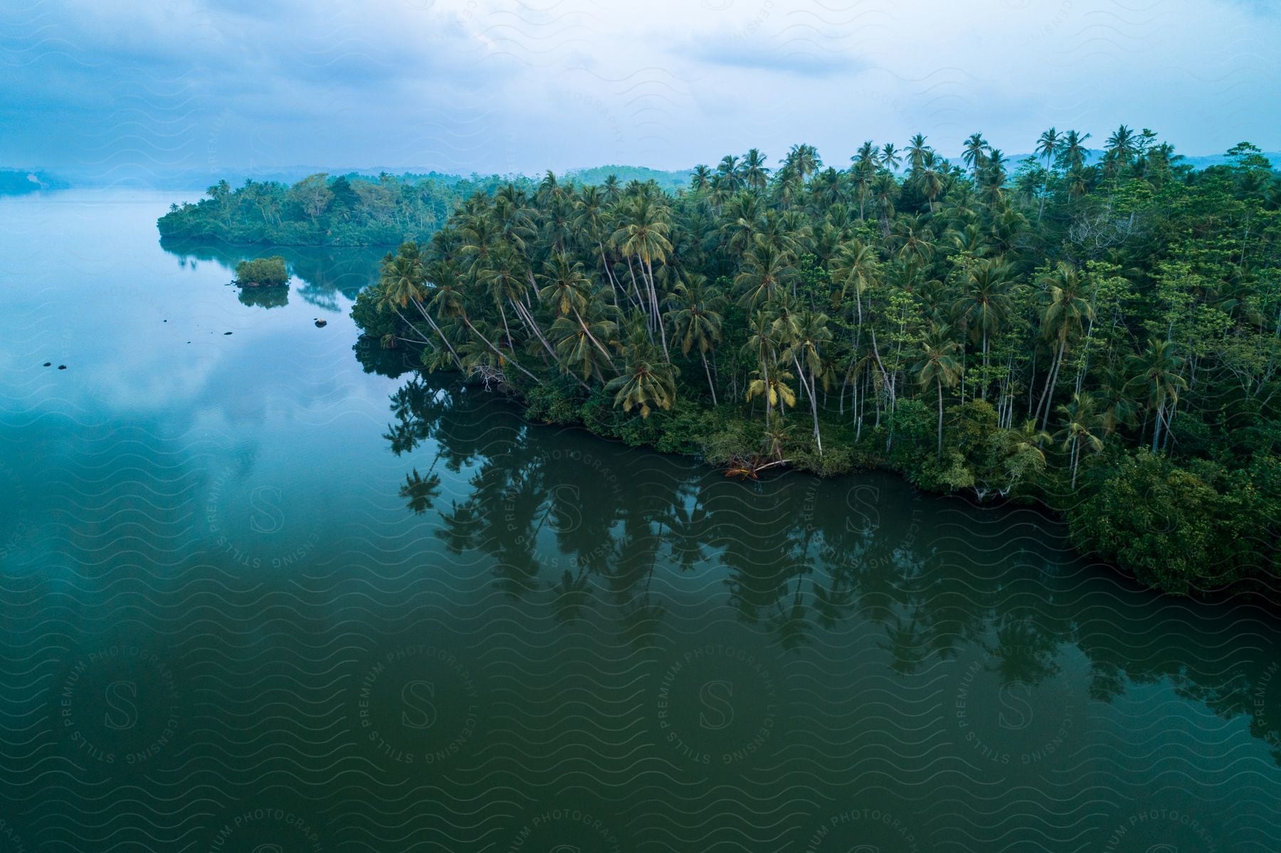 A few islands with lush green palm trees surrounded by aqua water under a blue cloudy sky.