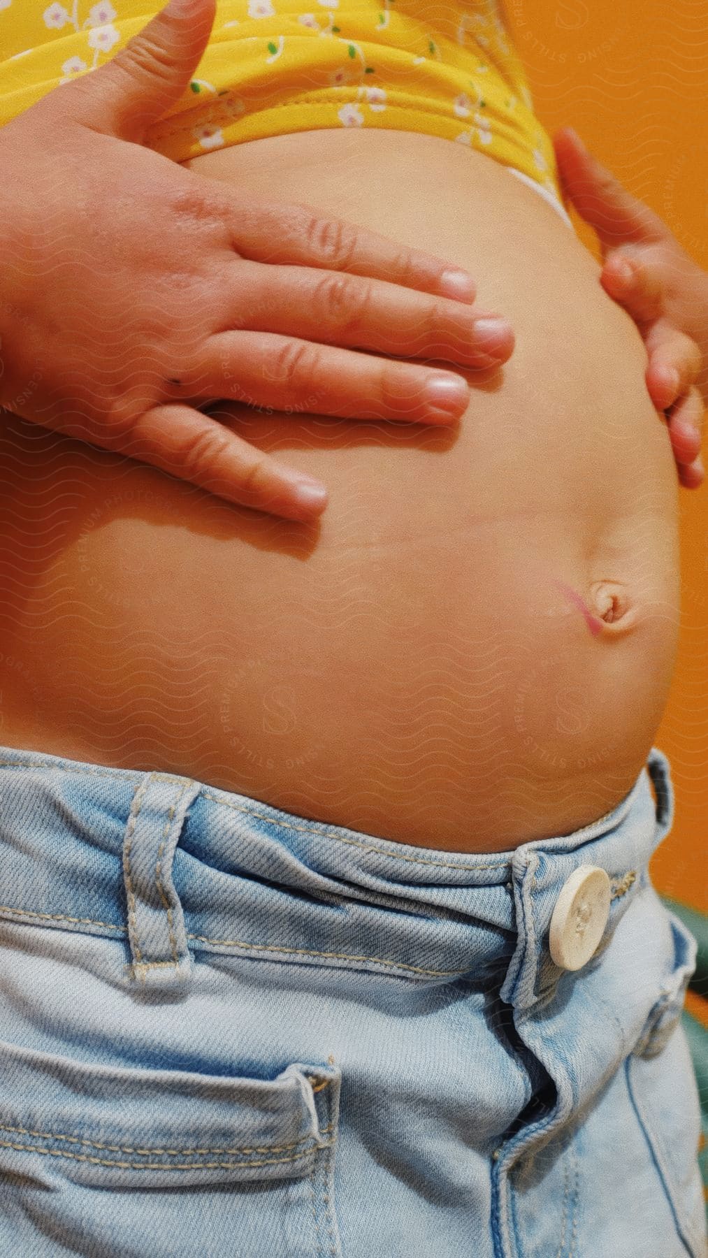 Female touches her bulging abdomen while standing in an orange walled room.