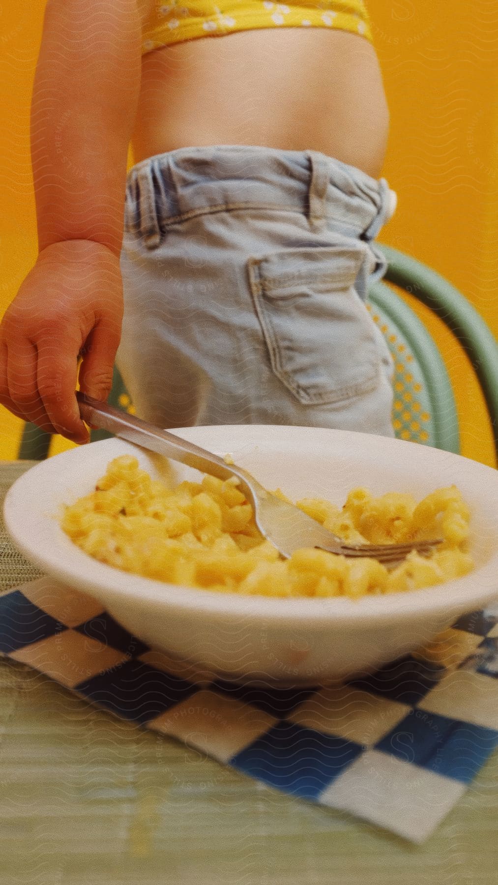 A waist of a person who is holding a fork that is inside a white bowl with yellow food