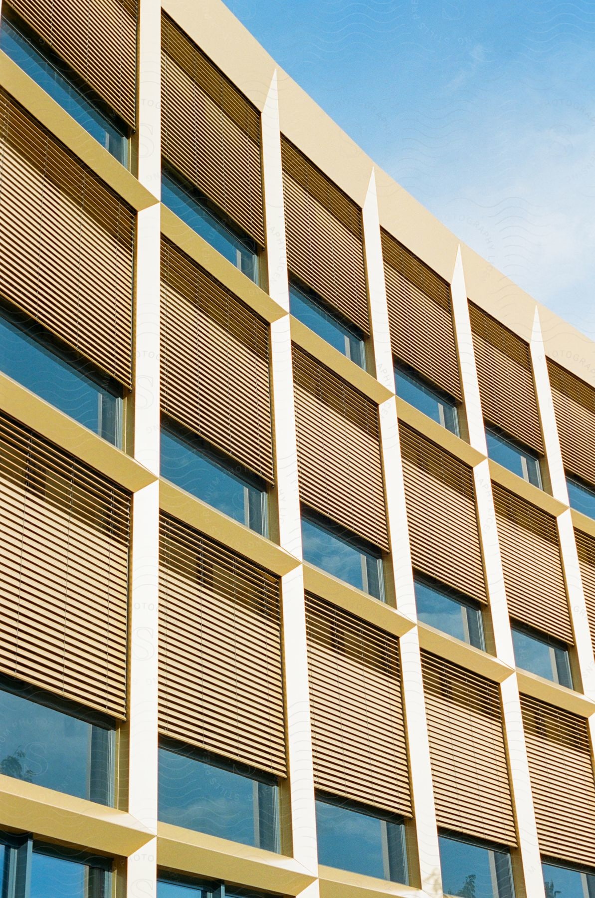 Facade of a modern building with rectangular windows and shutters.