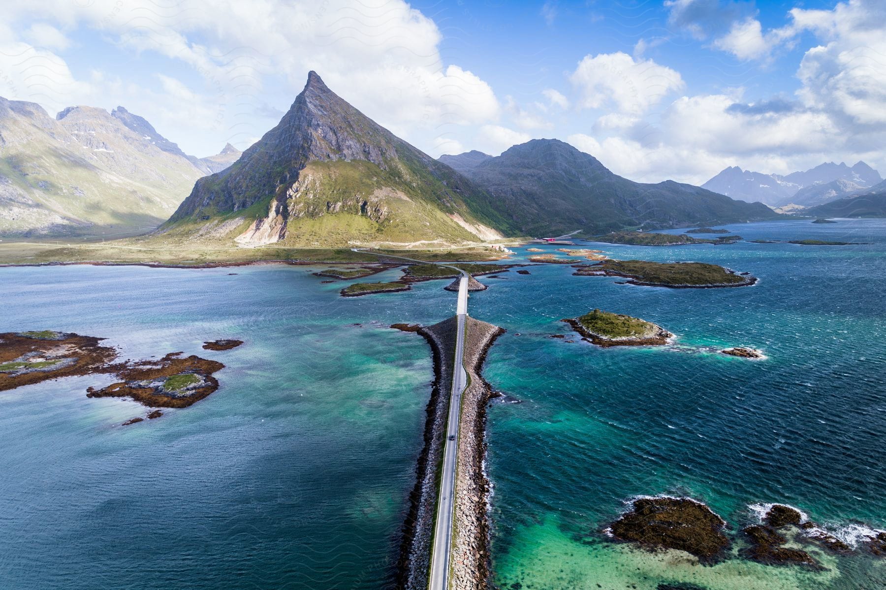 Aerial landscape of Fredvang Bridge over turquoise sea with mountains on the horizon