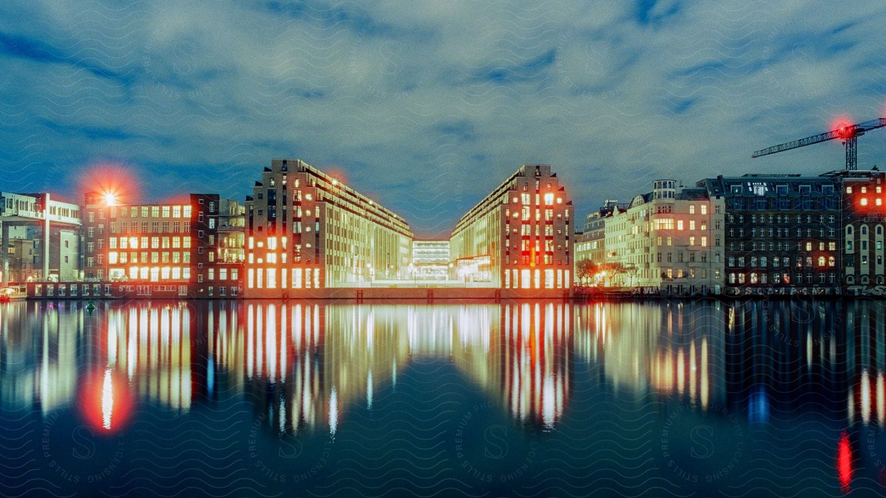 Bright building lights along the coast reflect on the water under a cloudy sky