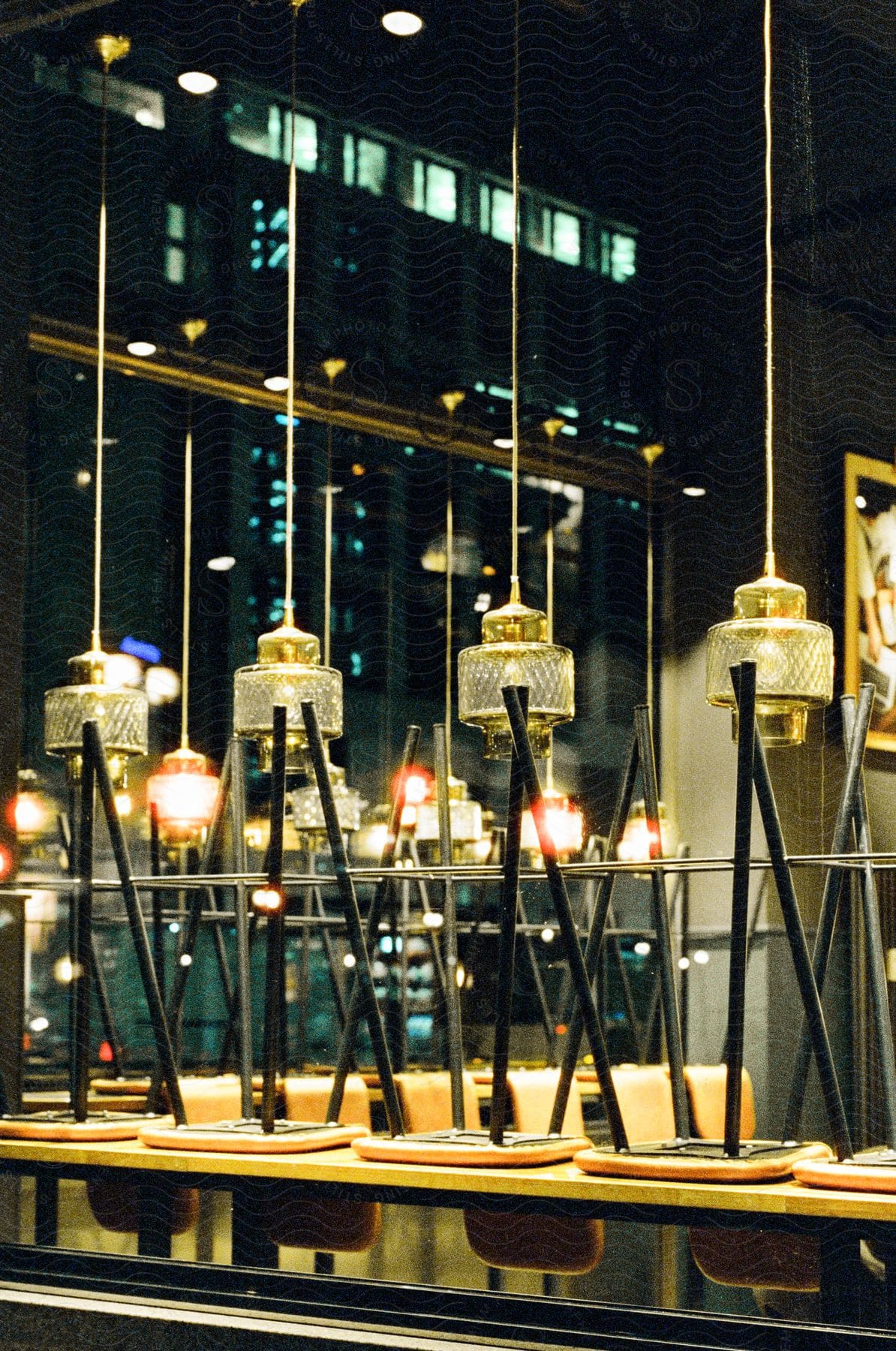 Several stools placed upside down on a wooden table and on top are chandeliers and behind there is a huge glass window showing a dark building.