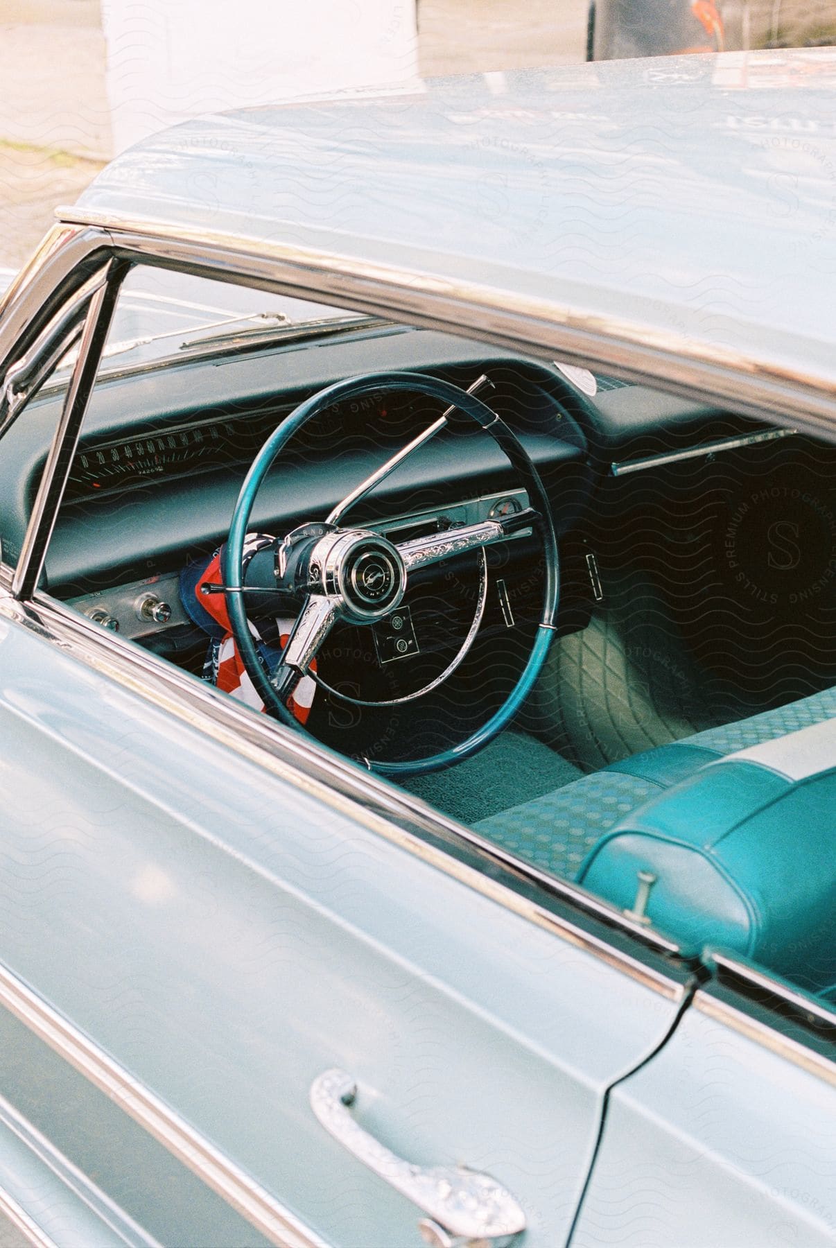 The steering wheel of a car, with its front seat interior visible from outside, and the front window down.