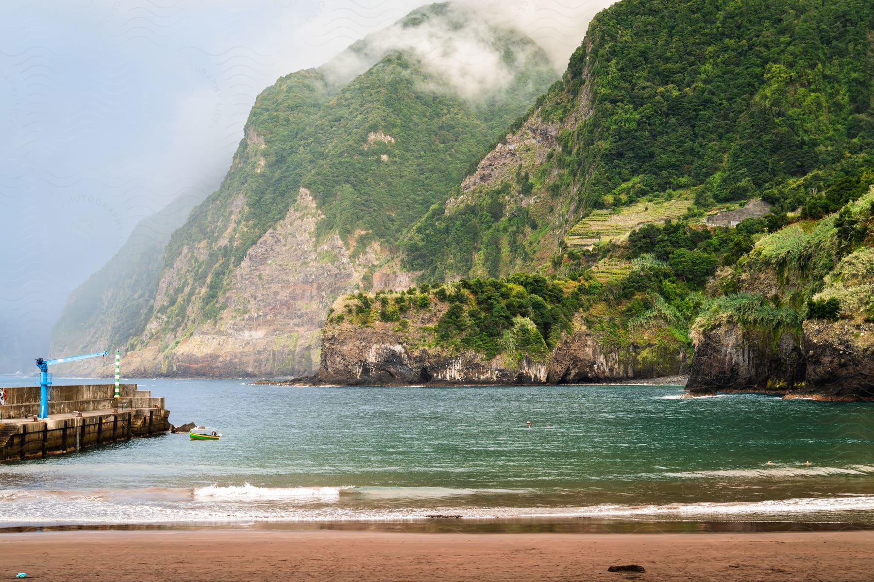 An island encircled by mountains, adorned with grassy terrain, with a boat moored near the beach during the day.