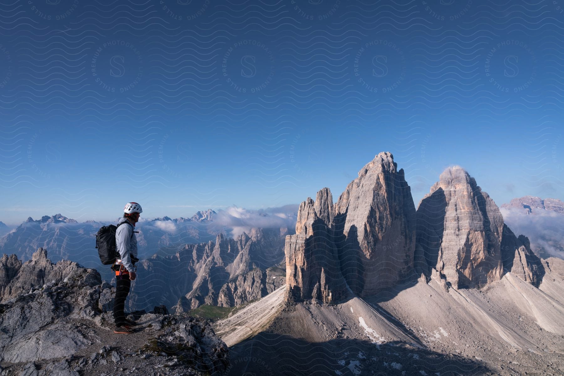 Hiker stands on a mountain ledge overlooking rock formations with mountains in the distance