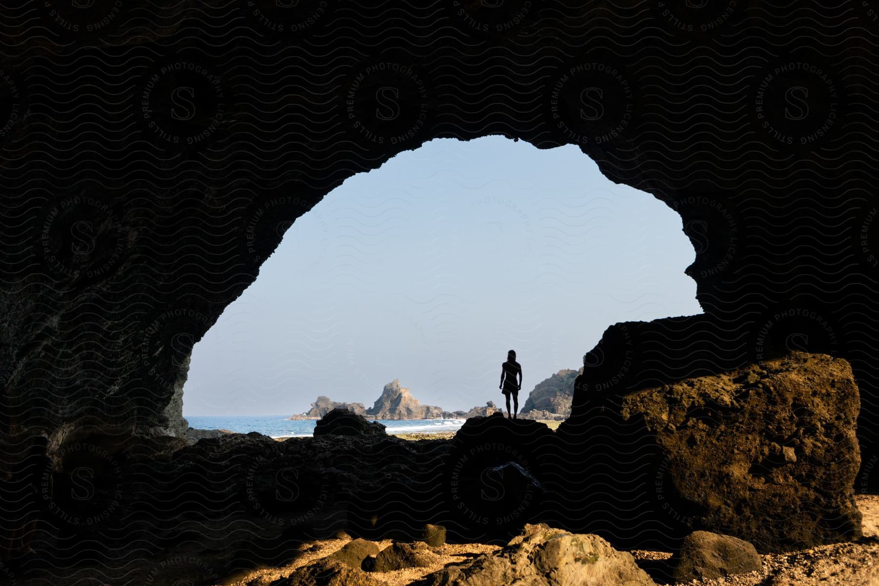 A person standing near a cove looking towards the sea with large rocks.