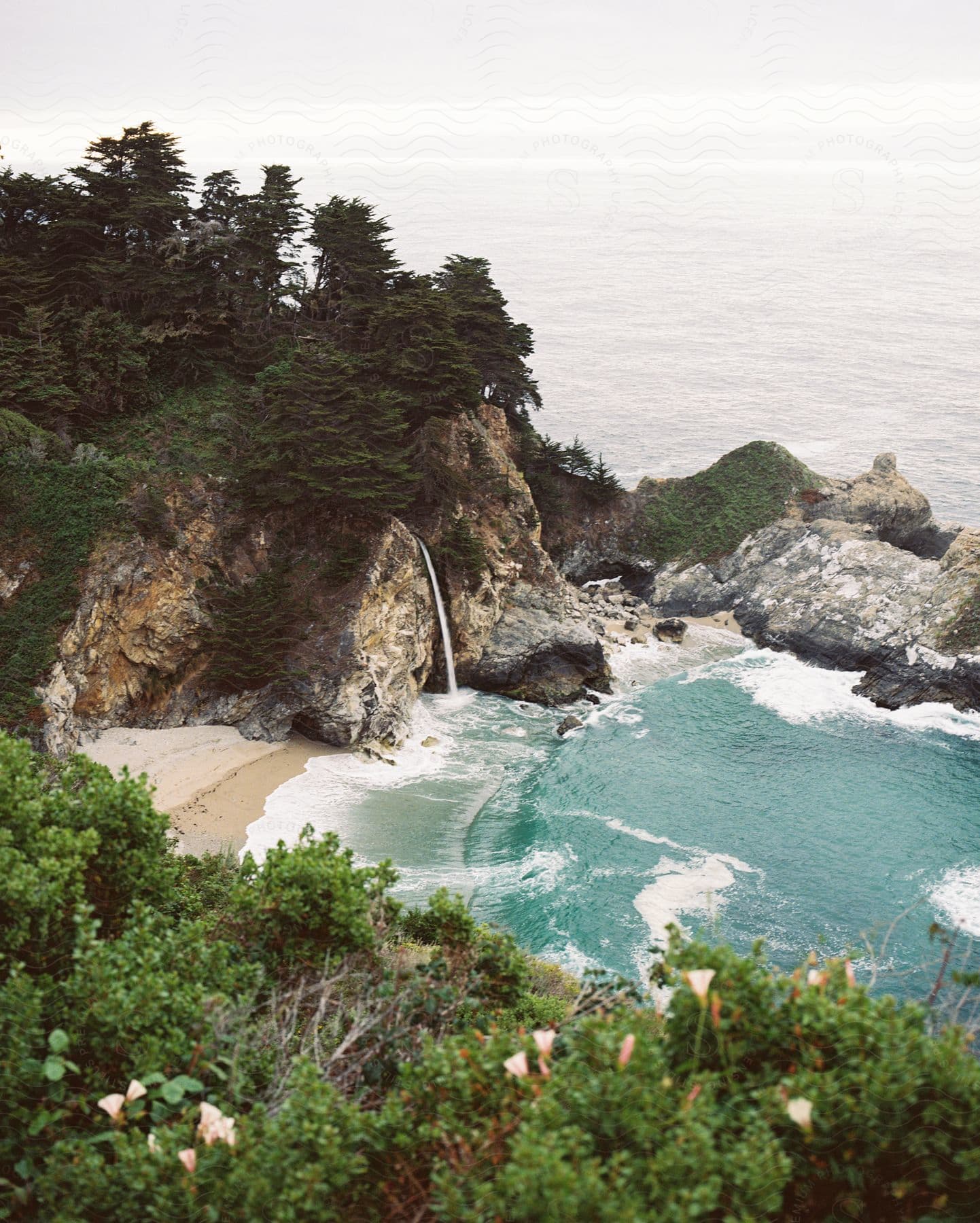 Landscape of a small beach with turquoise waters and the surrounding coast with waterfall and trees