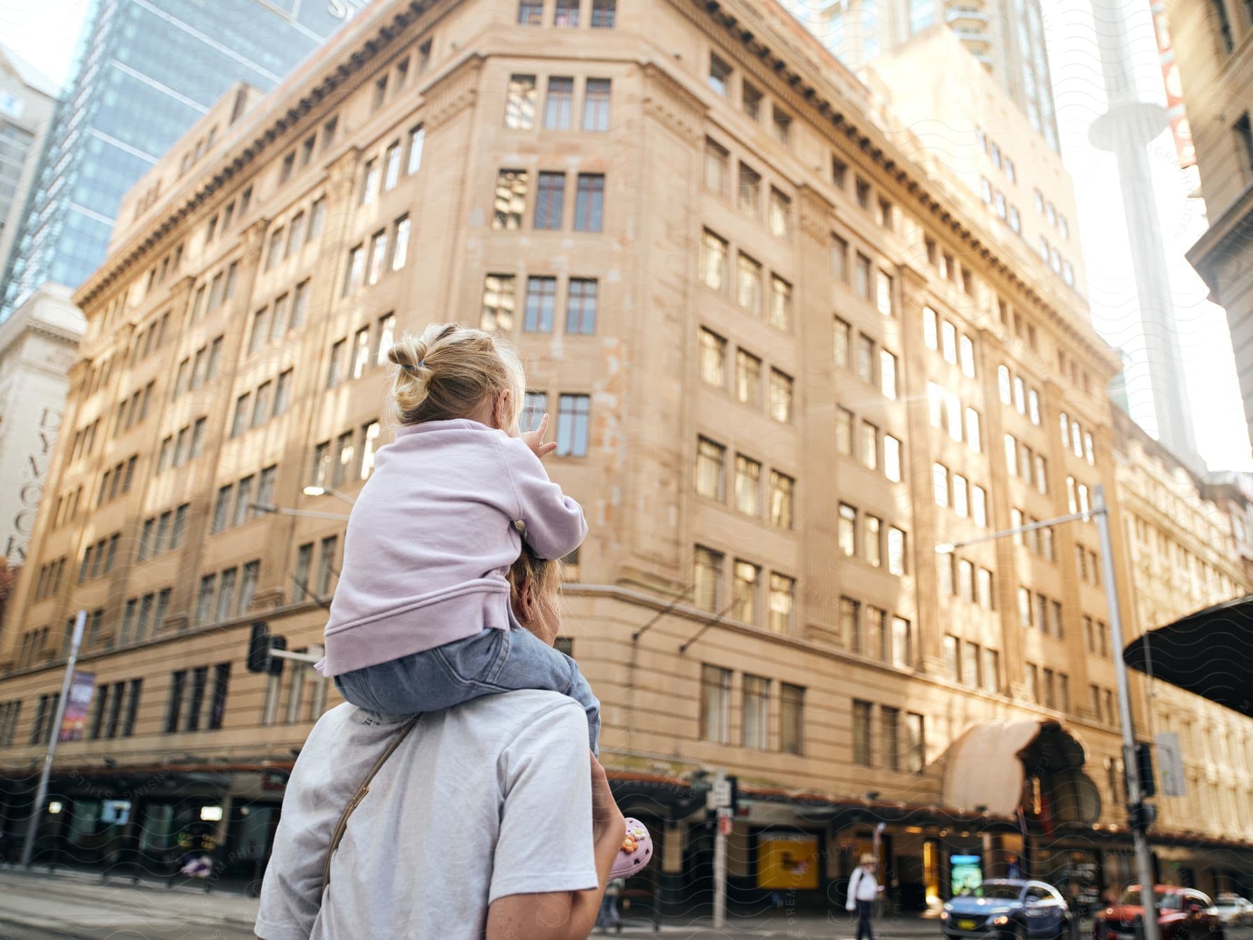 Child on an adult's shoulders looking at city buildings.