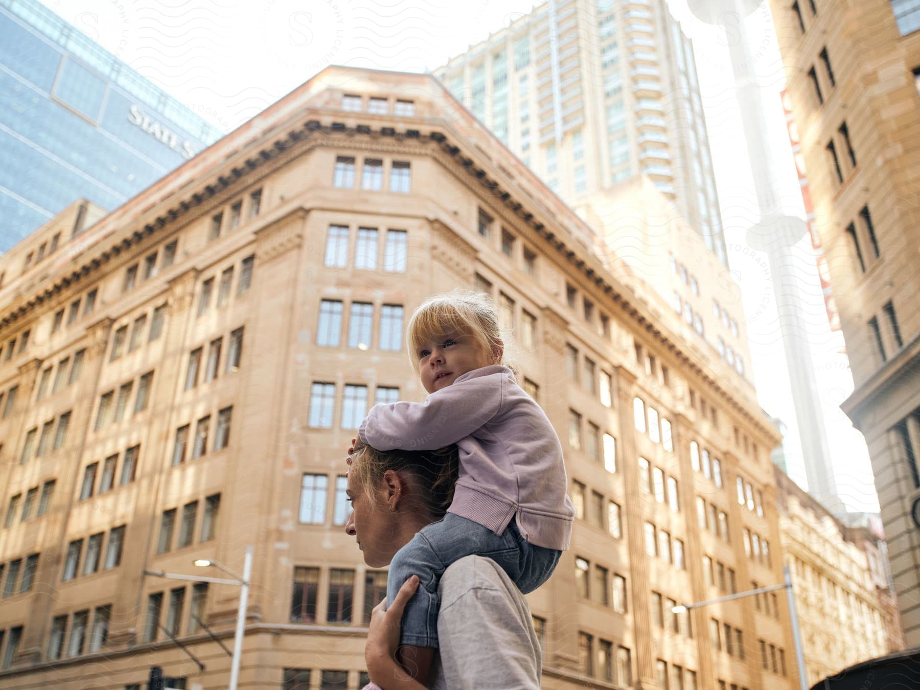 A little girl perched on her dad's shoulders, wide-eyed with wonder at the towering city buildings.