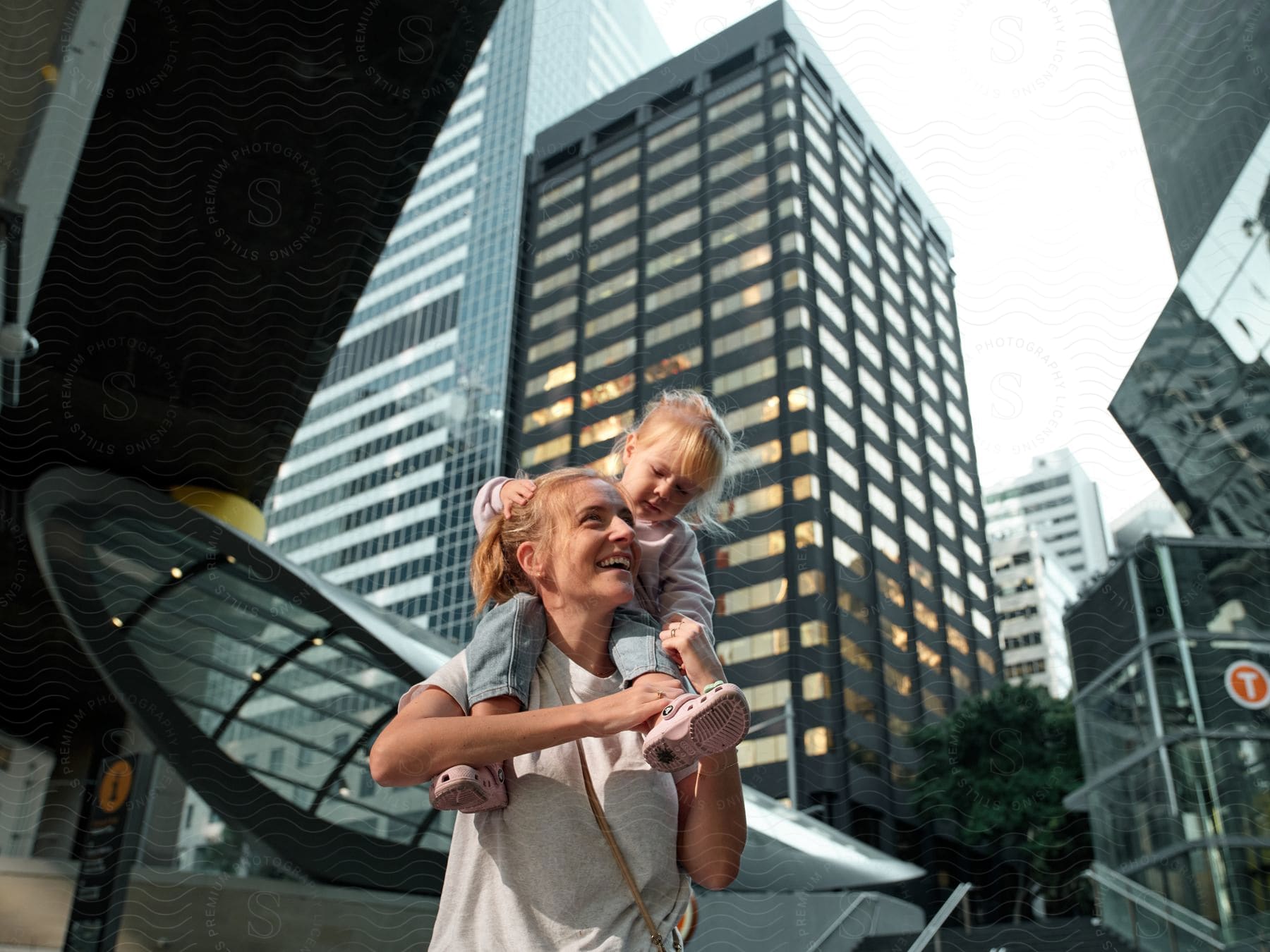 Little girl riding on her mother's shoulders as they walk among tall buildings and skyscrapers downtown