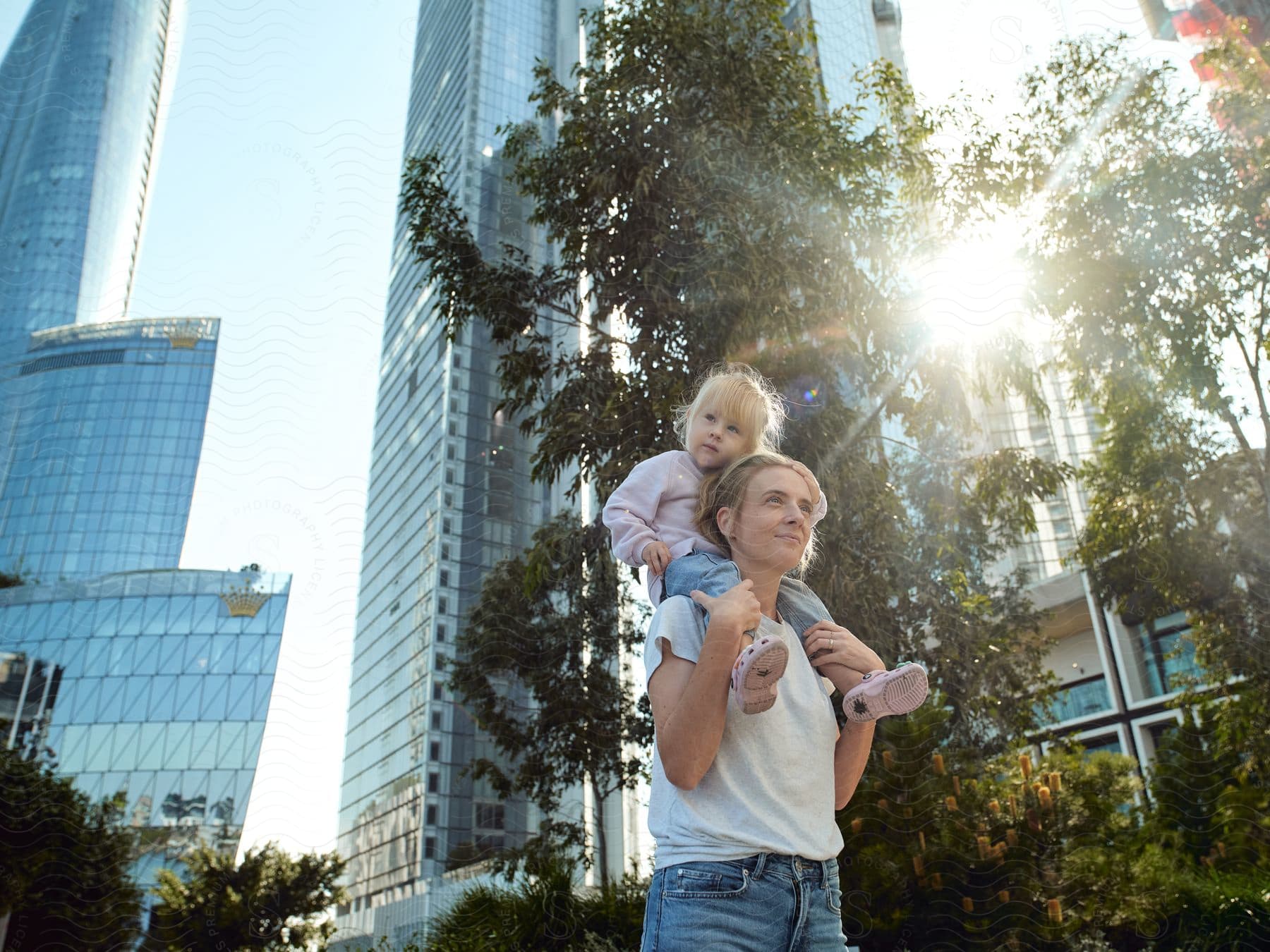 Adult with a child on shoulders enjoying a sunny day among tall city buildings.