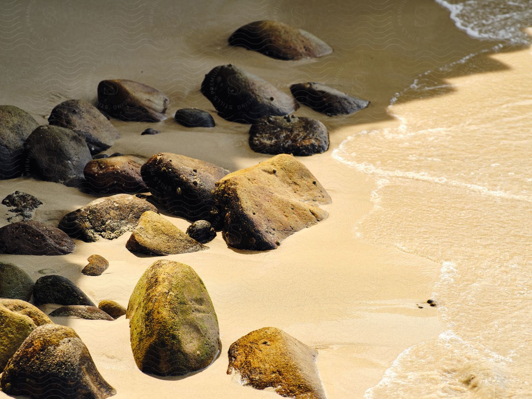 Several rocks buried in the sand of a beach with small ripples nearby