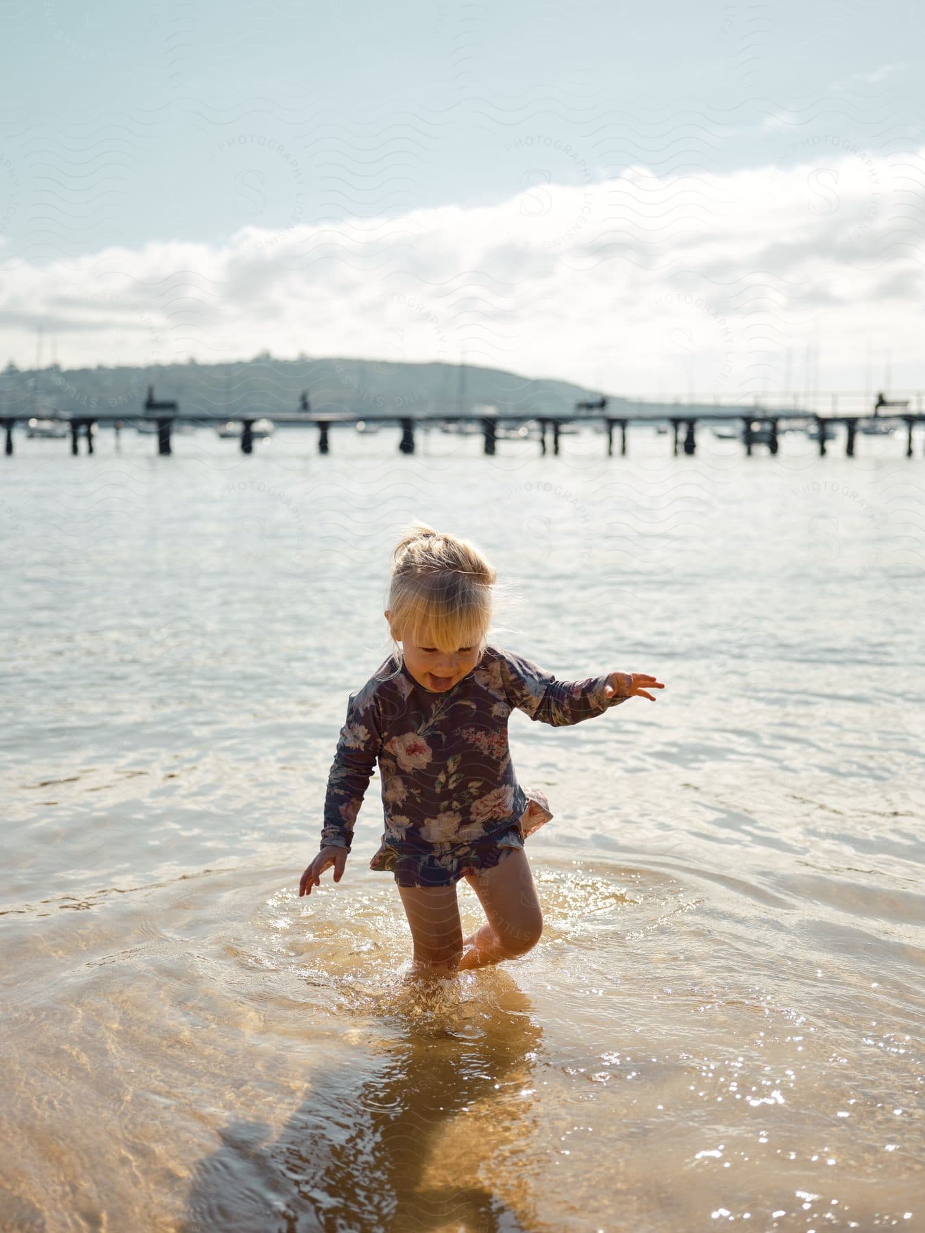 Little girl walking in shallow water with a pier and boats in the distance