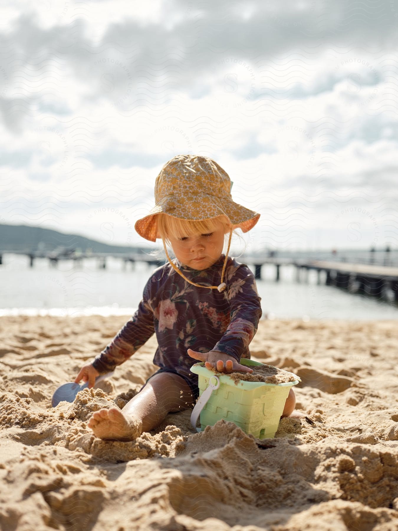 Toddler playing with a sand bucket and shovel on the beach during the day.