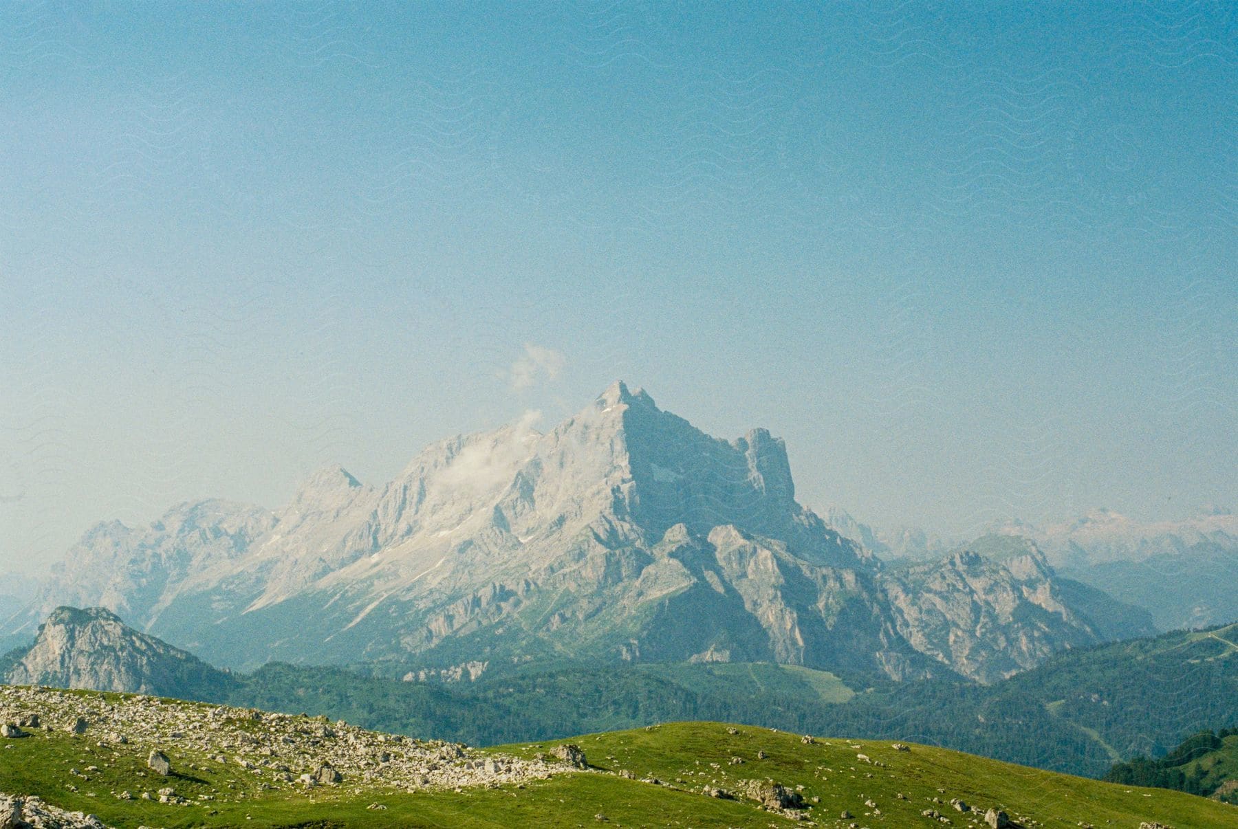 A huge white mountain on the horizon and in front of large white hills with vegetation and forest