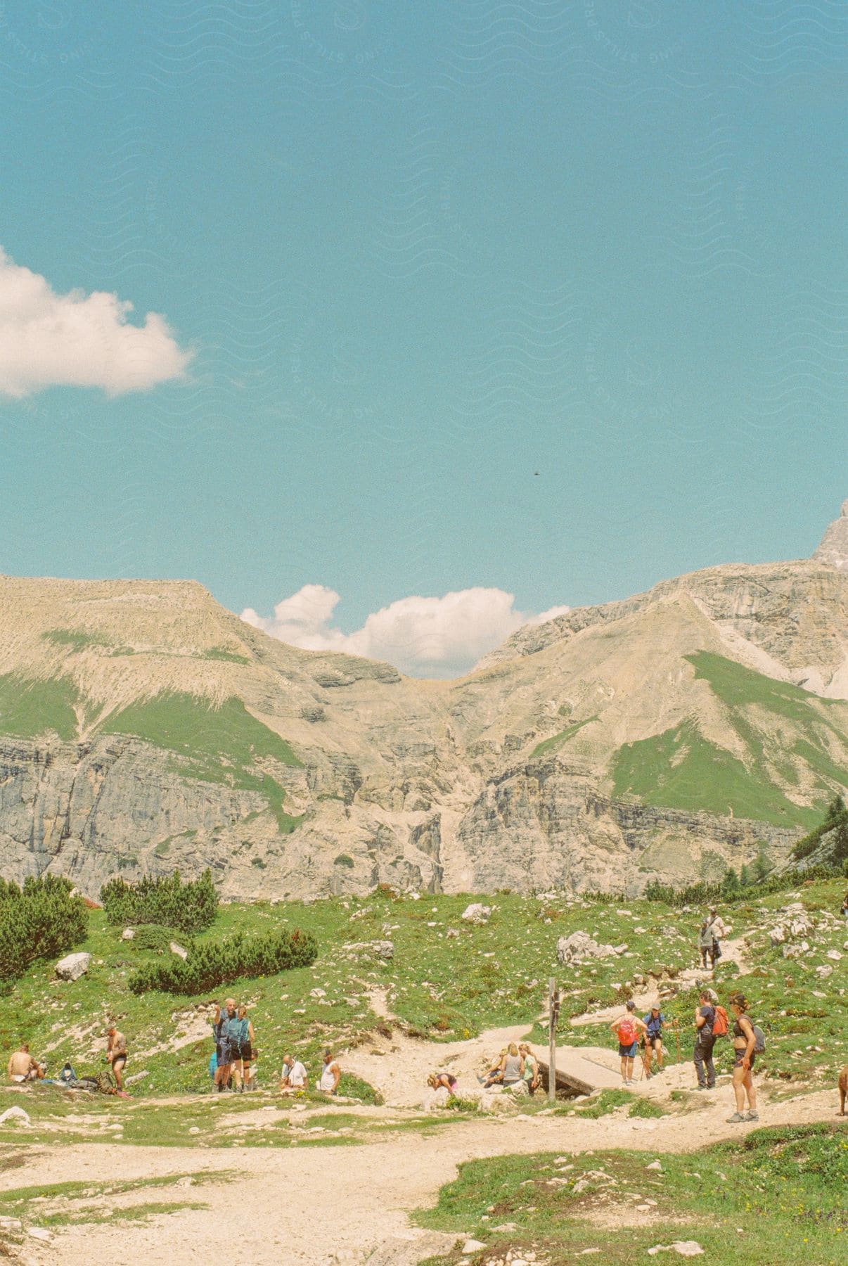 Group of people walking on a mountainous trail under a blue sky with clouds.