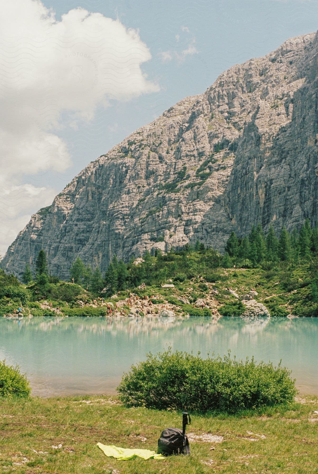 Turquoise water lake surrounded by vegetation and a rocky mountain in the background under a blue sky with clouds.