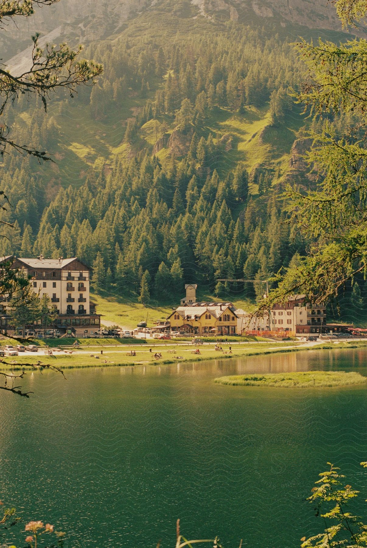 Greenish lake surrounded by mountains with vegetation and rustic buildings on the shore.
