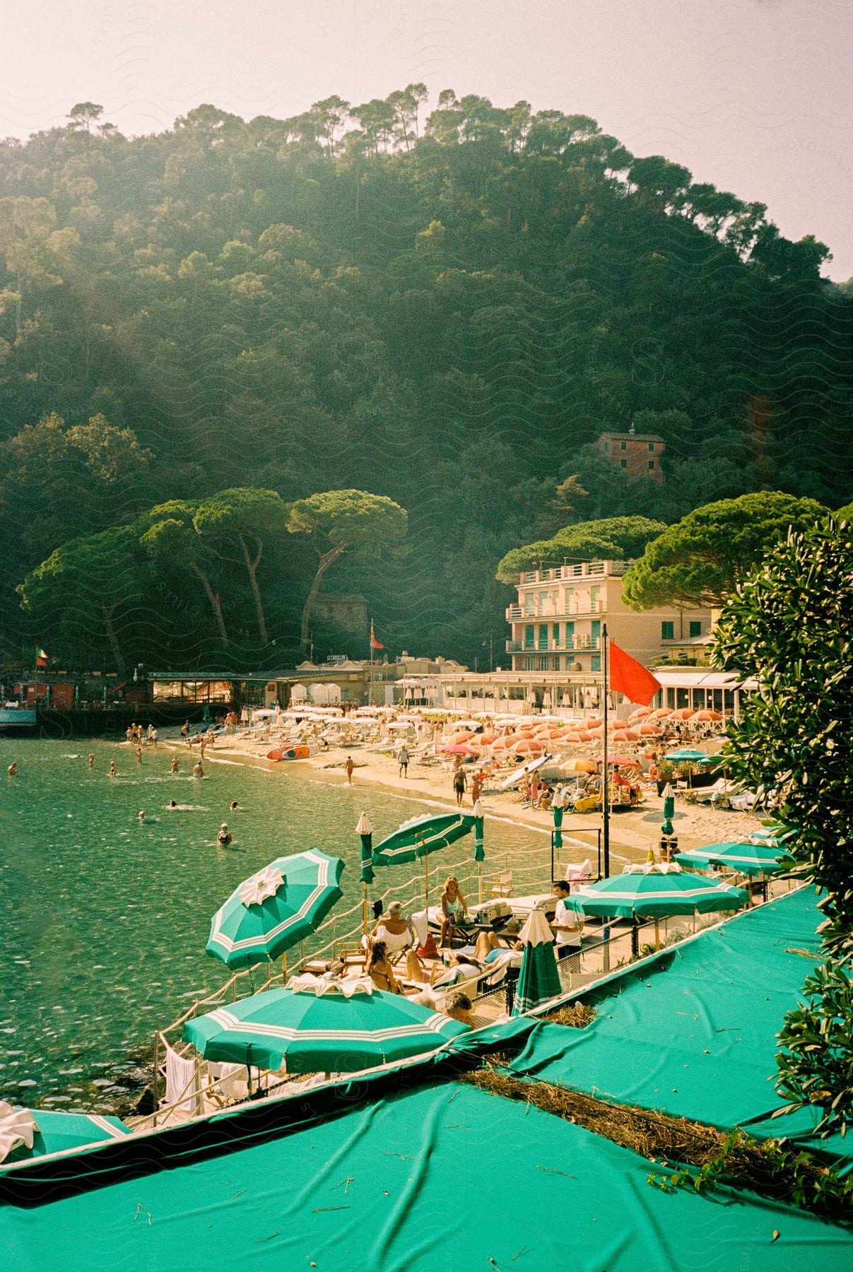 A beach is active with tourists swimming and dinning on a sunny day.