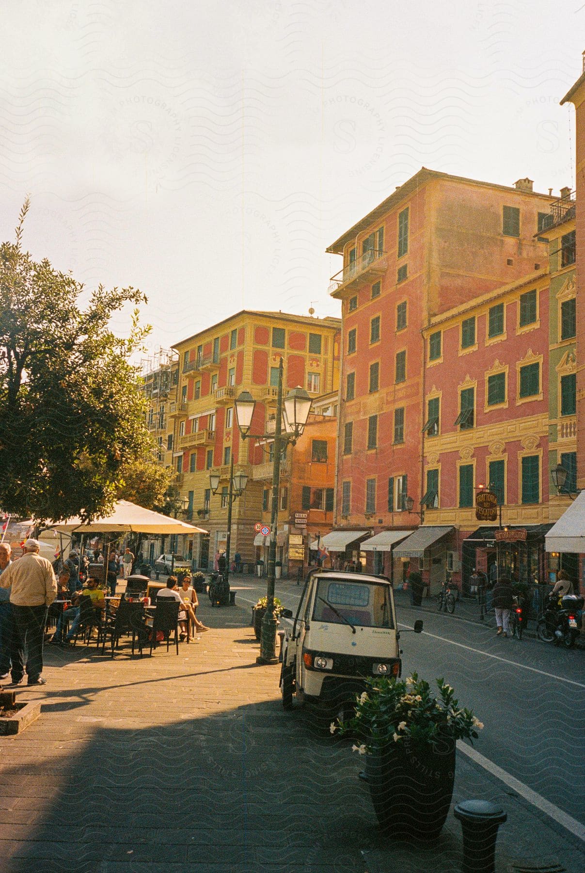 Busy street during the day with buildings and people strolling in shops along the sidewalks.