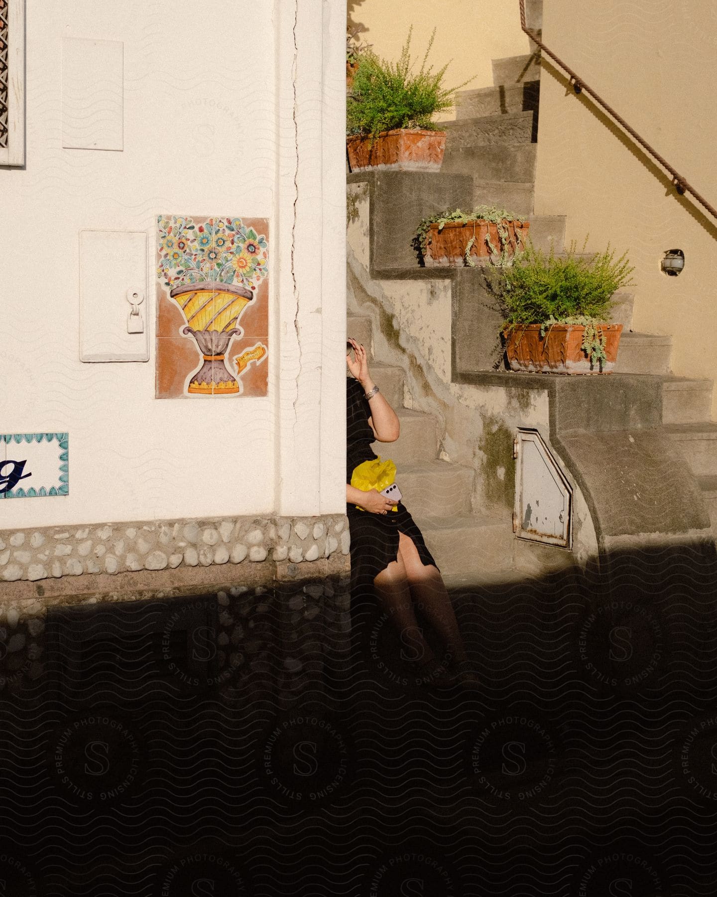 External architecture of a white wall with artistic sequins and the legs of a woman sitting next to it on the stairs.