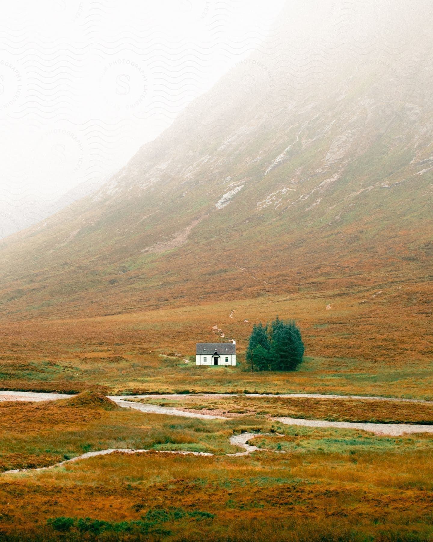 A small white house sits at the base of a mountain on a foggy day.