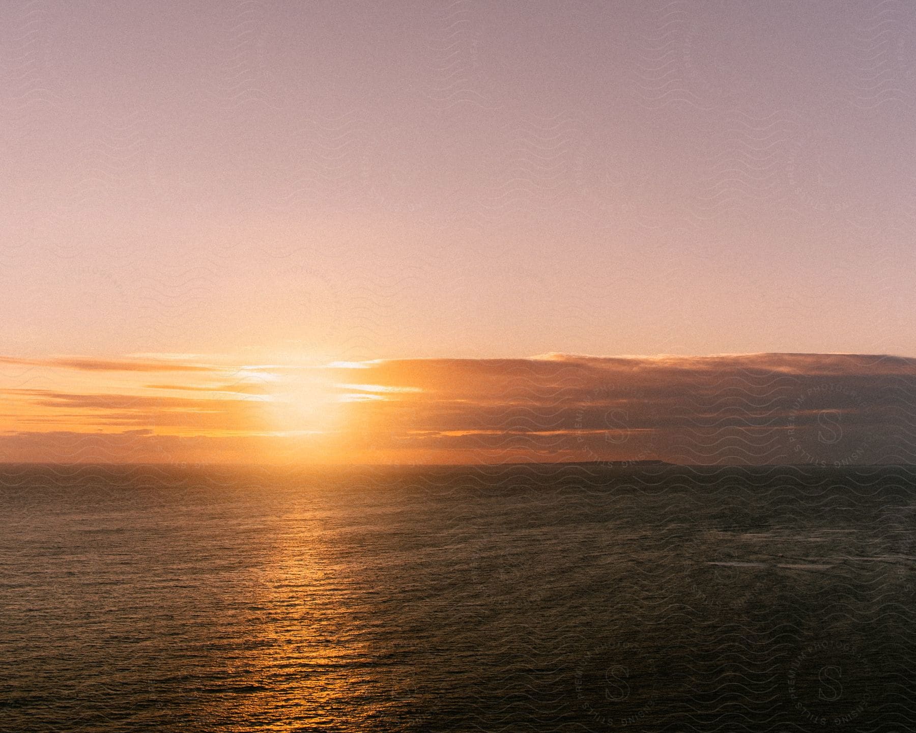 The ocean under a dusk sunset on a calm day.