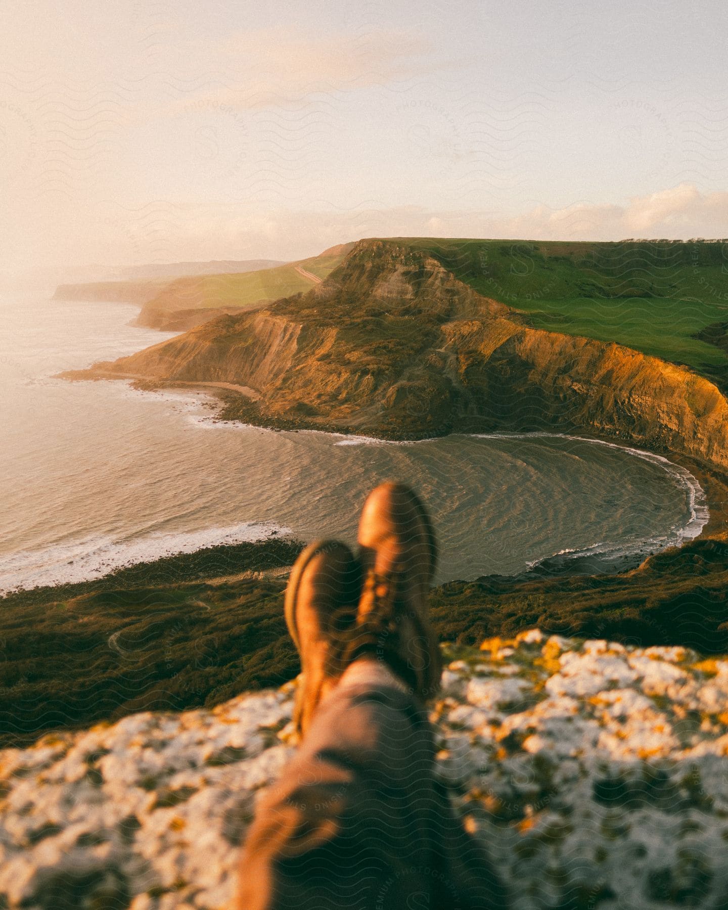 Point of view of a person's feet sitting on a rock at the top of a mountain with a panoramic view of a peninsula with the sea lapping at the sea coast