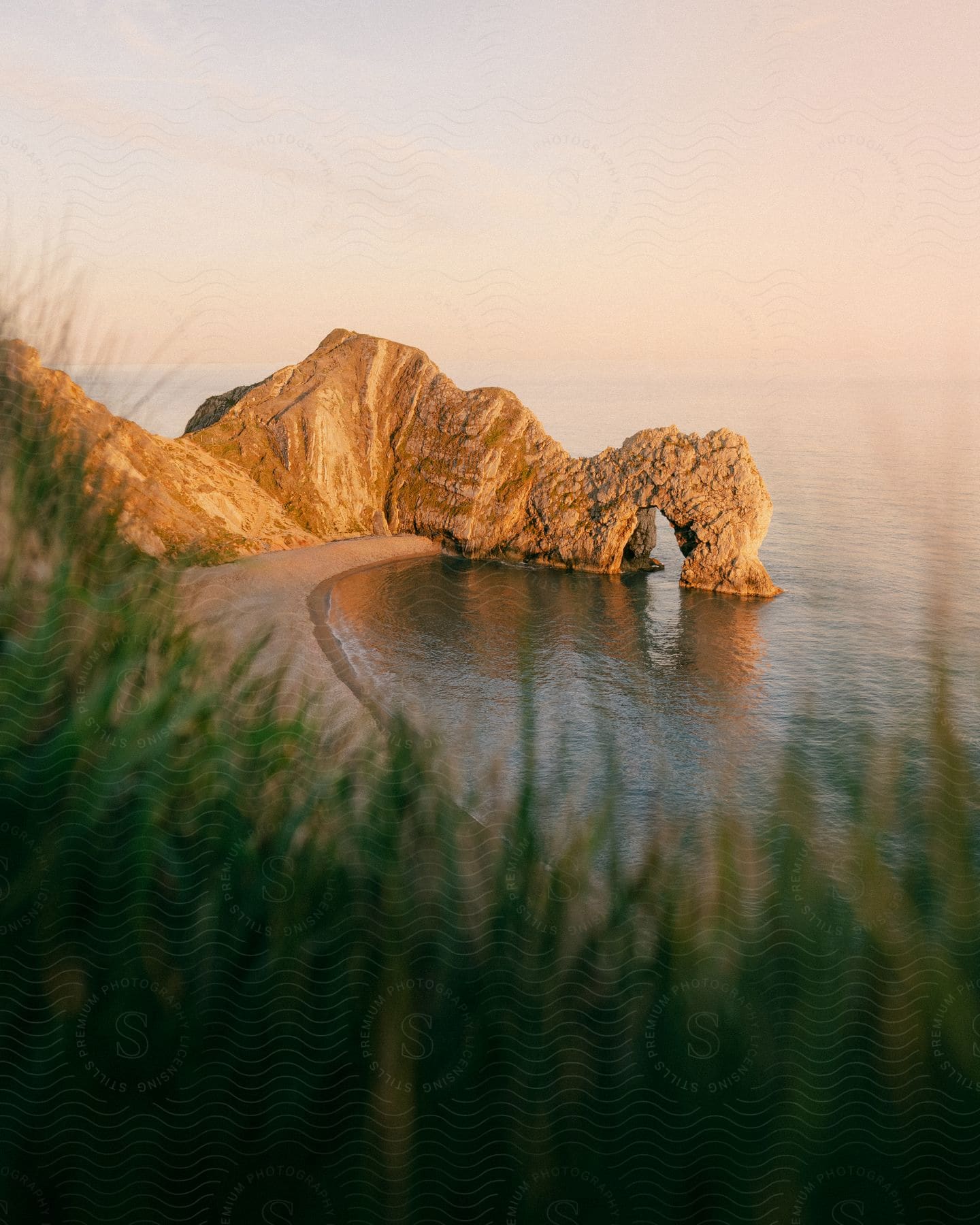 An ocean promontory contains a natural arch on a mostly cloudy day.