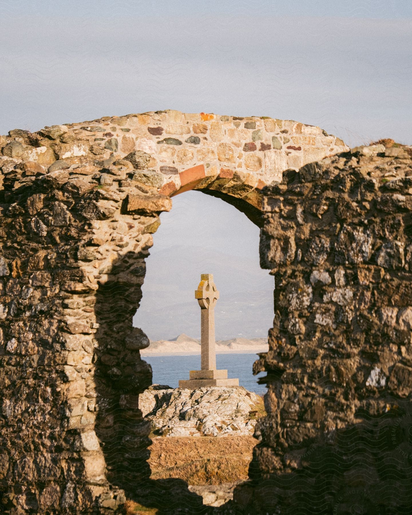 Stone cross seen through an opening in a stone wall with the sea in the background on the island of Ynys Llanddwyn