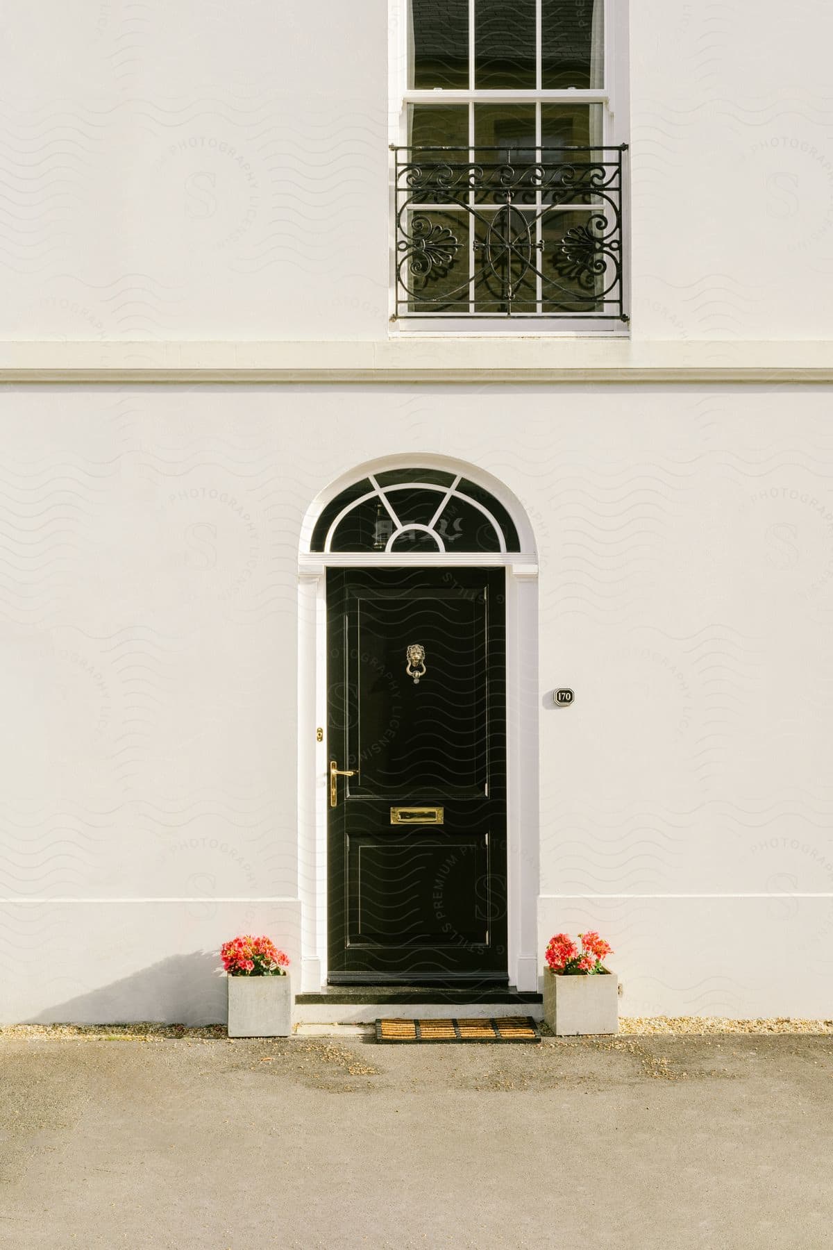 A dark green door on an all-white exterior wall with two flowers on the sides